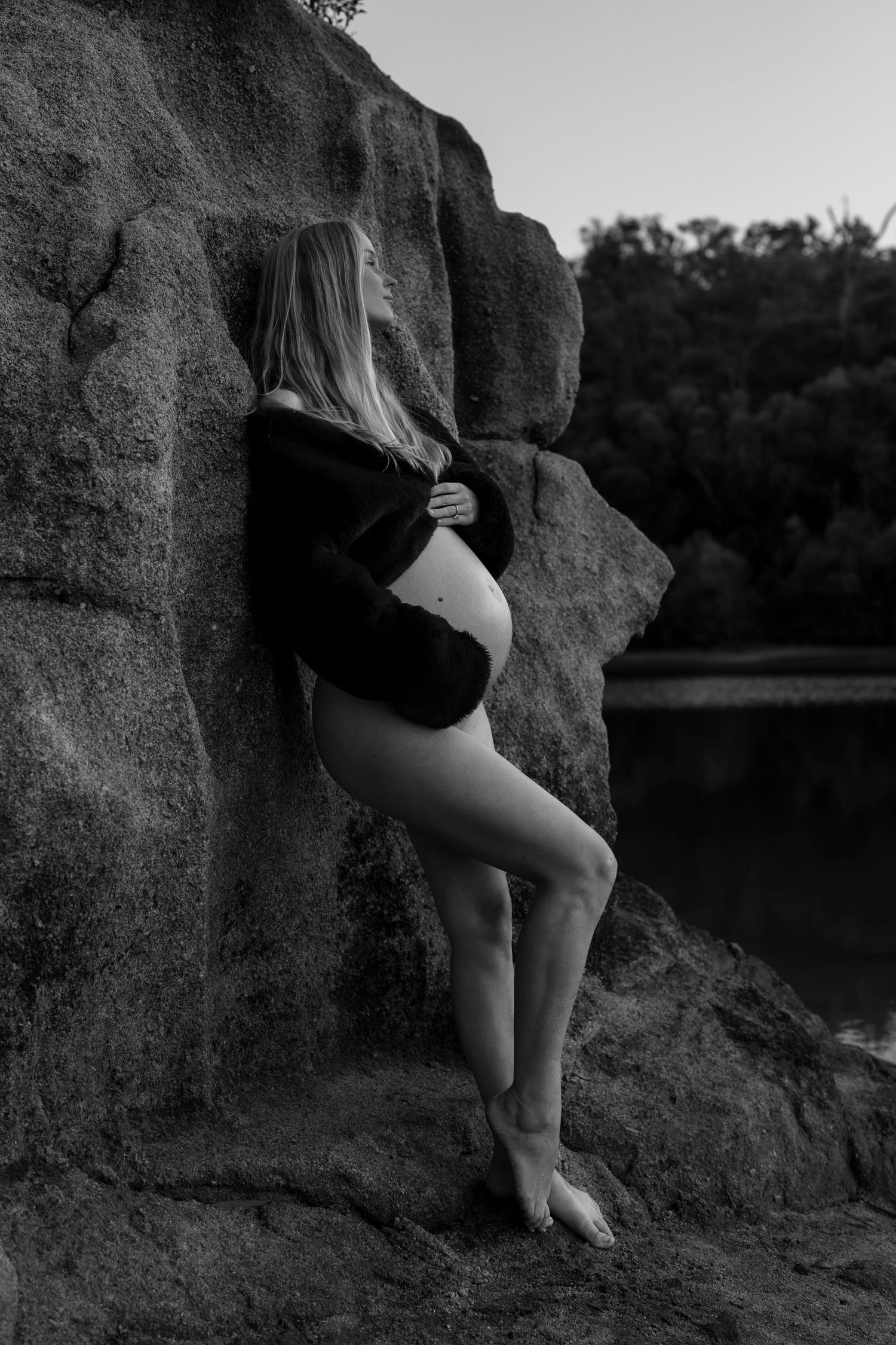 Black and white maternity portrait against natural rock formation by a lake.