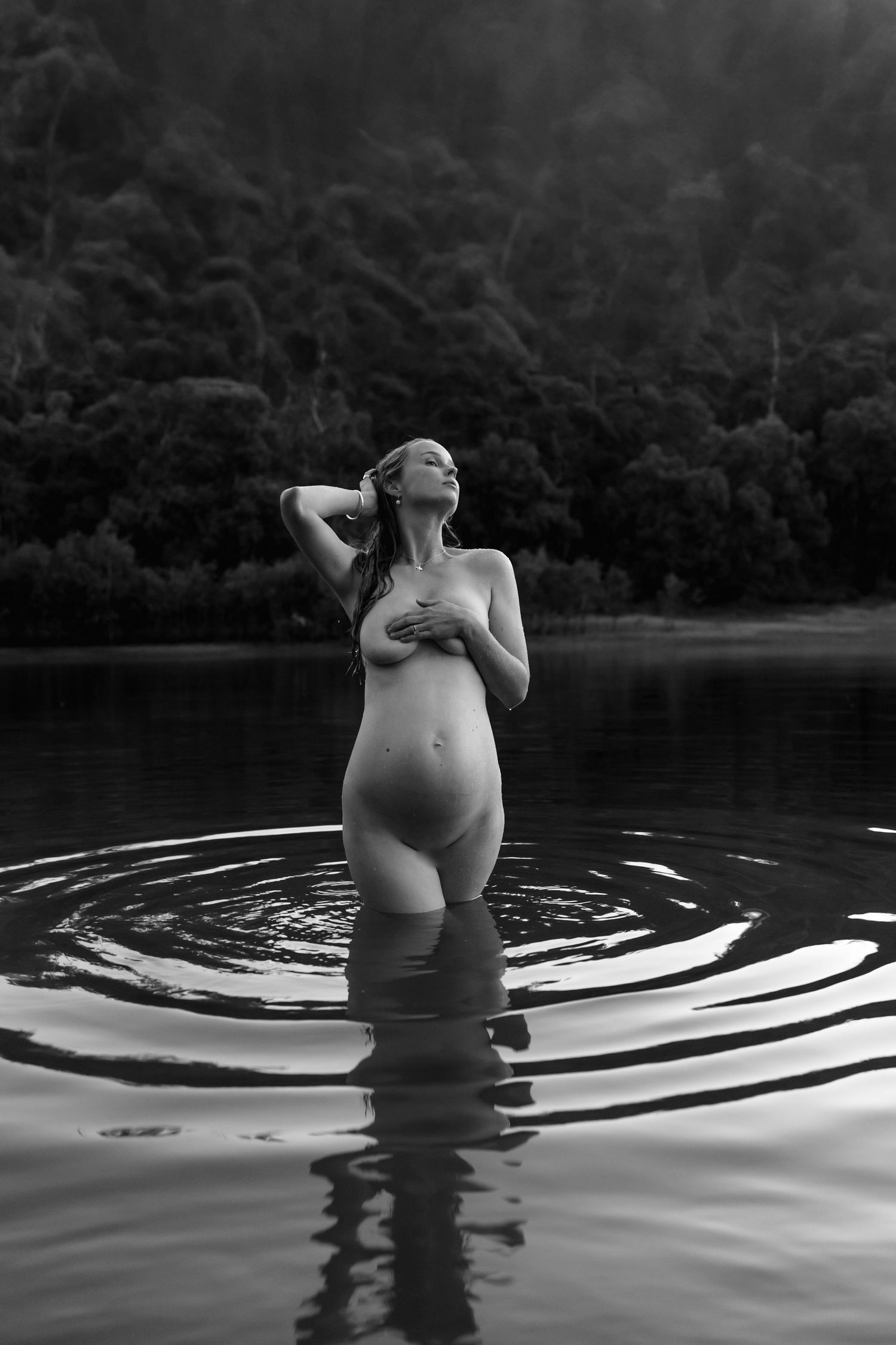 Black and white artistic maternity photo capturing reflections in still lake water.