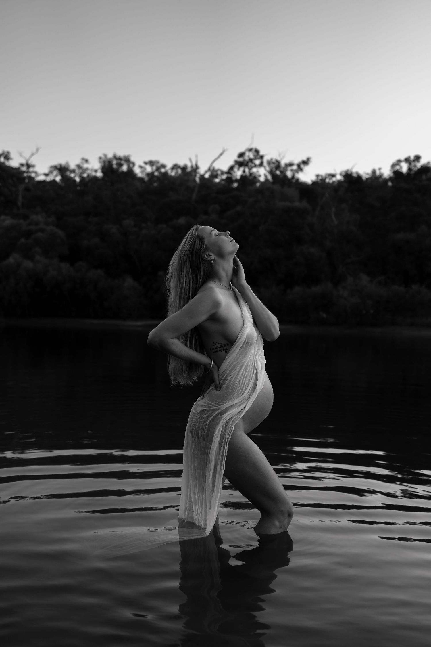 Ethereal black and white photo of a figure in sheer fabric standing in still water at dusk.