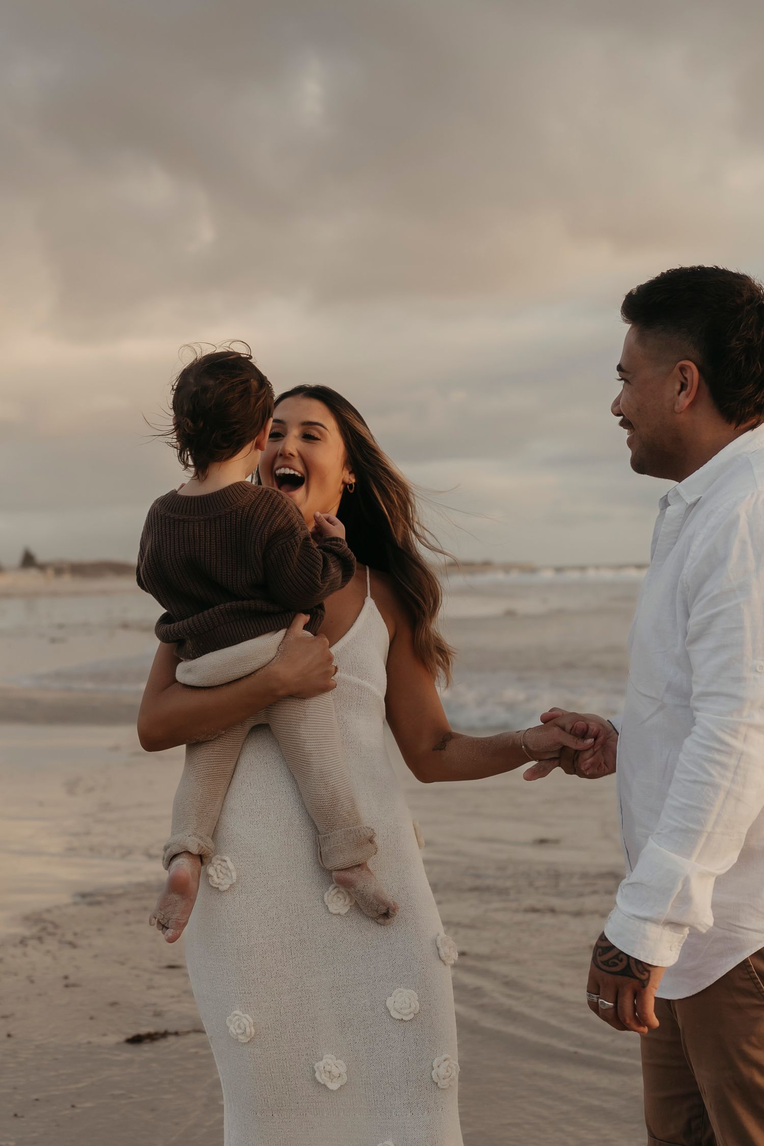 A happy family of three shares a joyful moment together while walking on a beach at sunset.