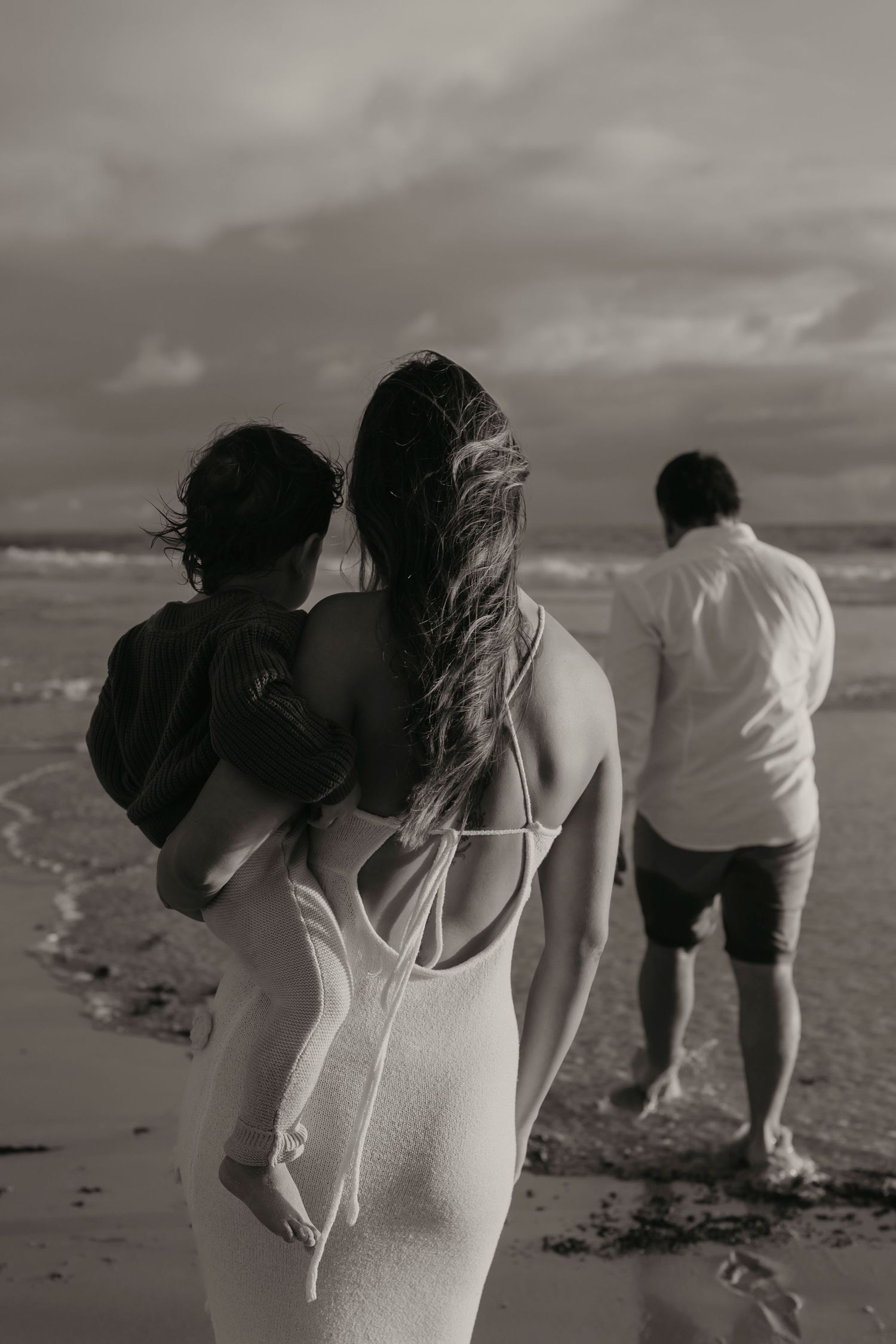 Moody black and white beach scene showing three figures strolling along the shoreline.