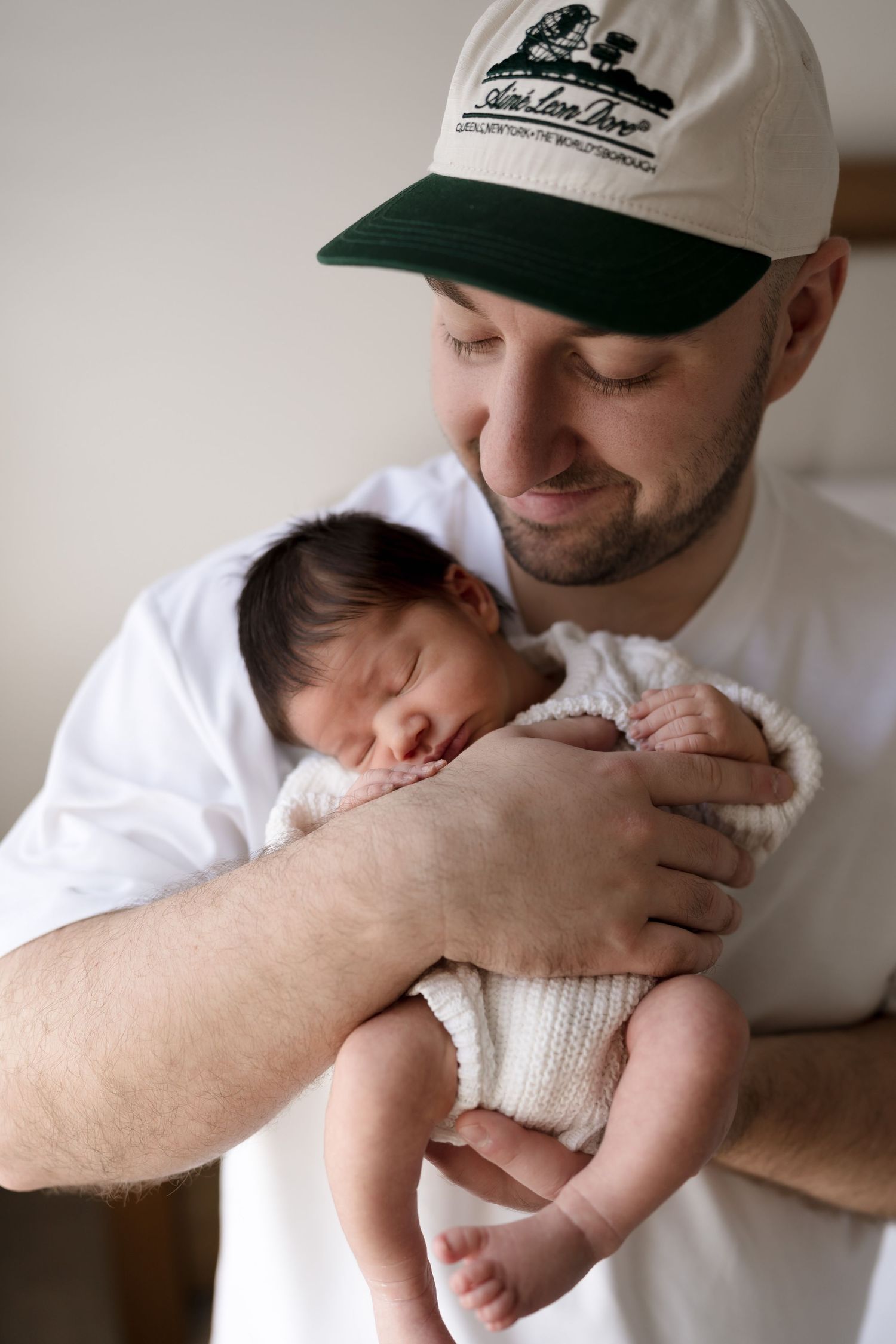 A tender moment of a newborn baby sleeping in their knitted onesie being cradled in protective arms.