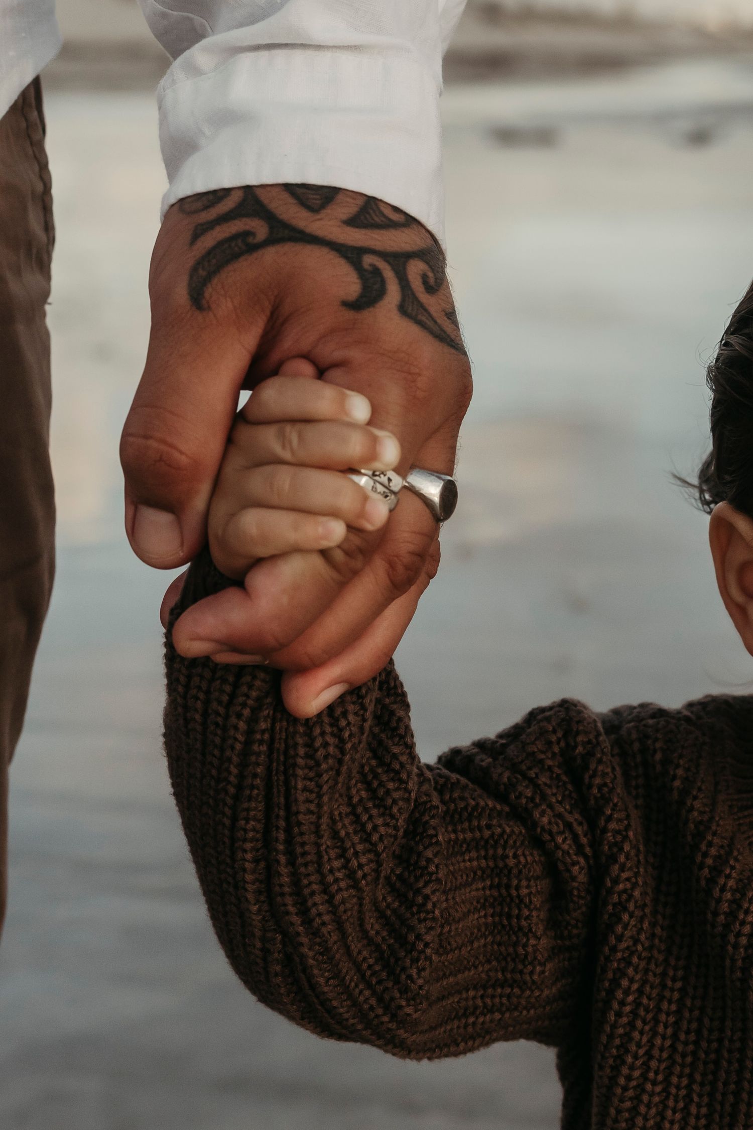 Close-up of two hands holding each other, one with tribal tattoo wearing white sleeve and engagement ring.