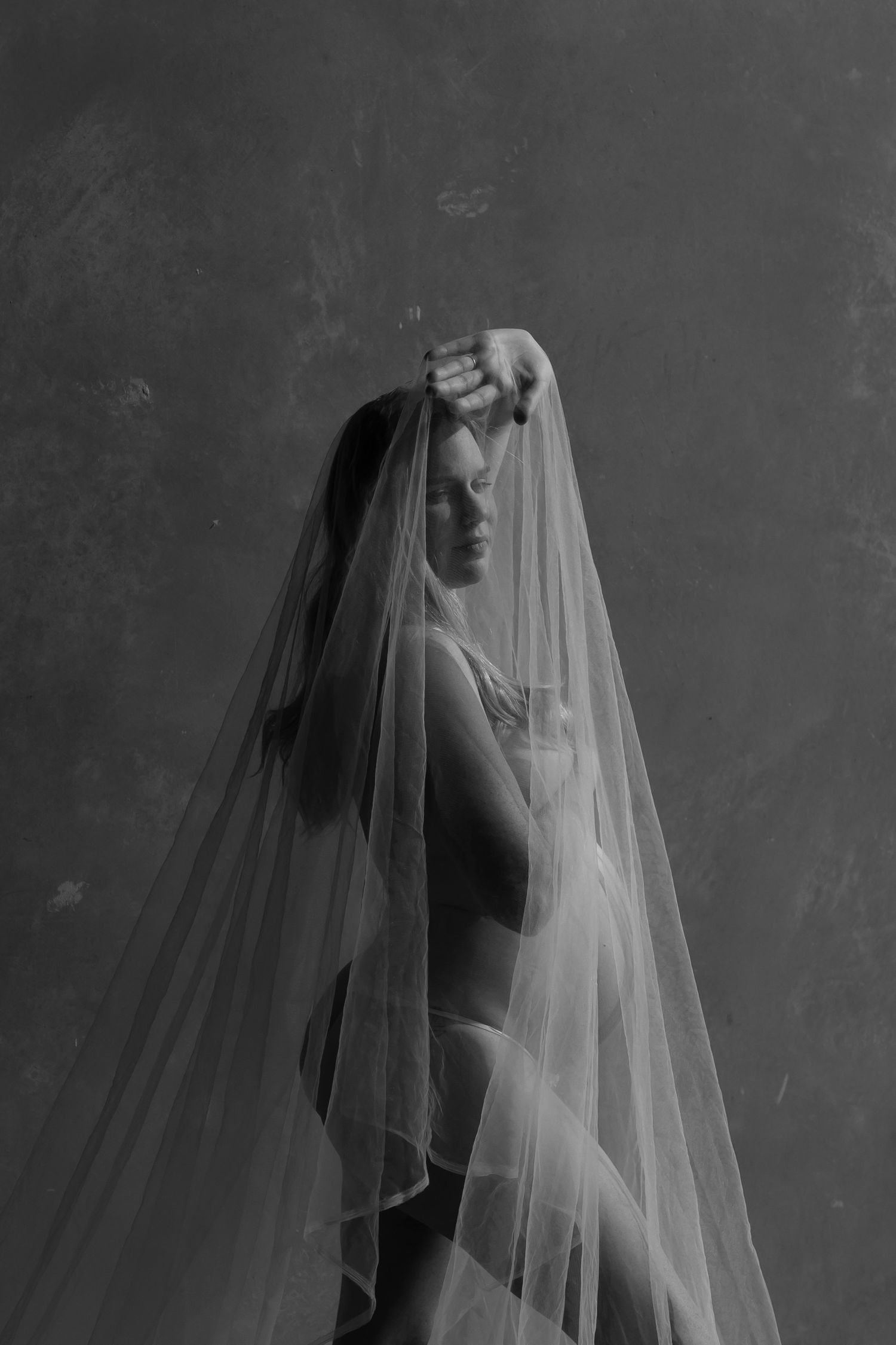 Black and white portrait of a bride elegantly draped in a flowing wedding veil, studio photography.