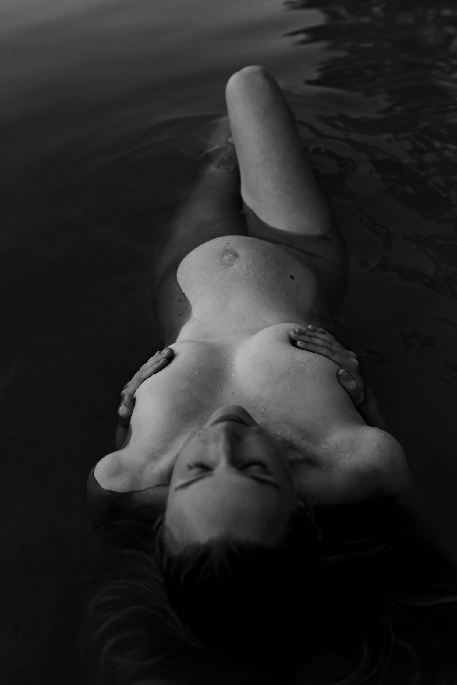 Artistic black and white portrait of a figure floating serenely in dark water.