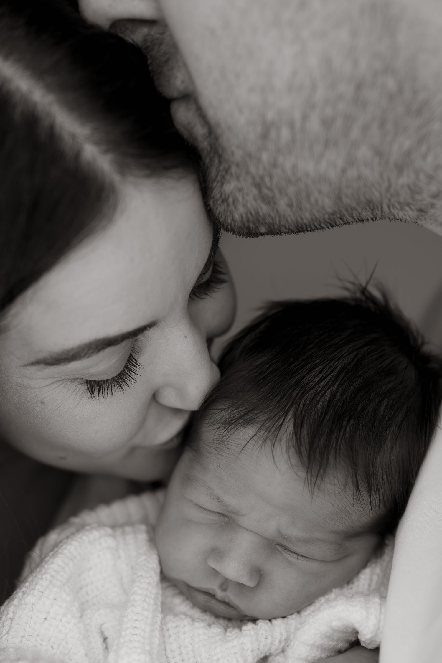 A tender black and white portrait of parent and newborn sharing an intimate moment.
