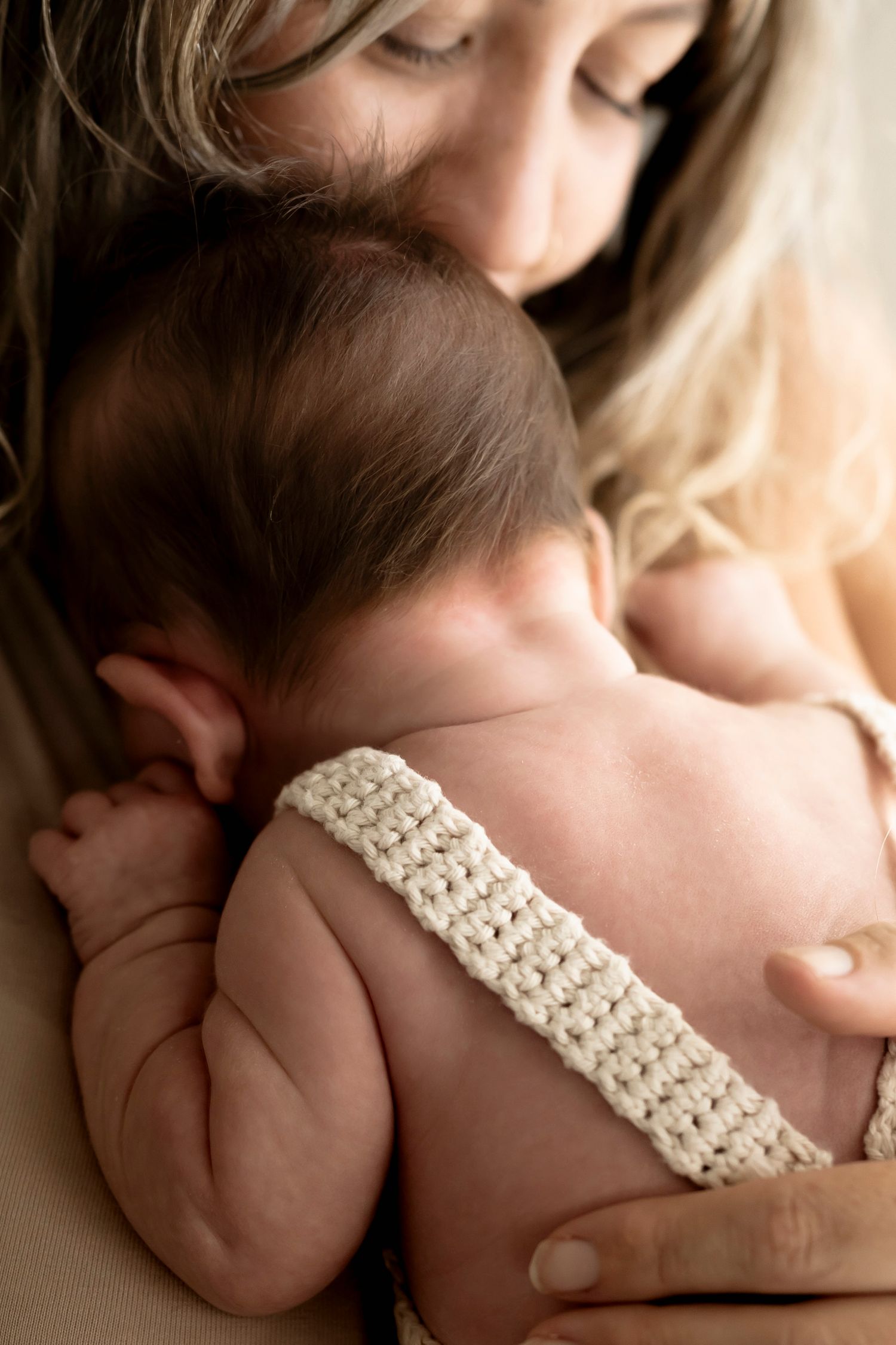 A tender moment of a mother cradling her newborn baby wearing a crochet headband against her chest.