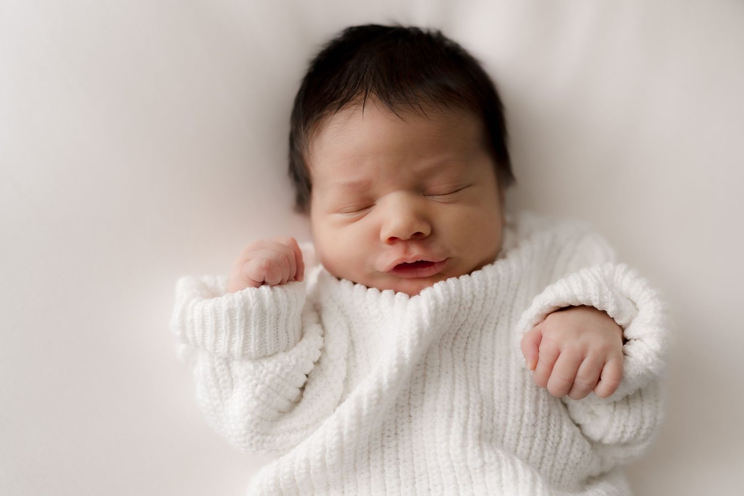 Peaceful sleeping newborn baby wearing soft white knitted sweater on light background.