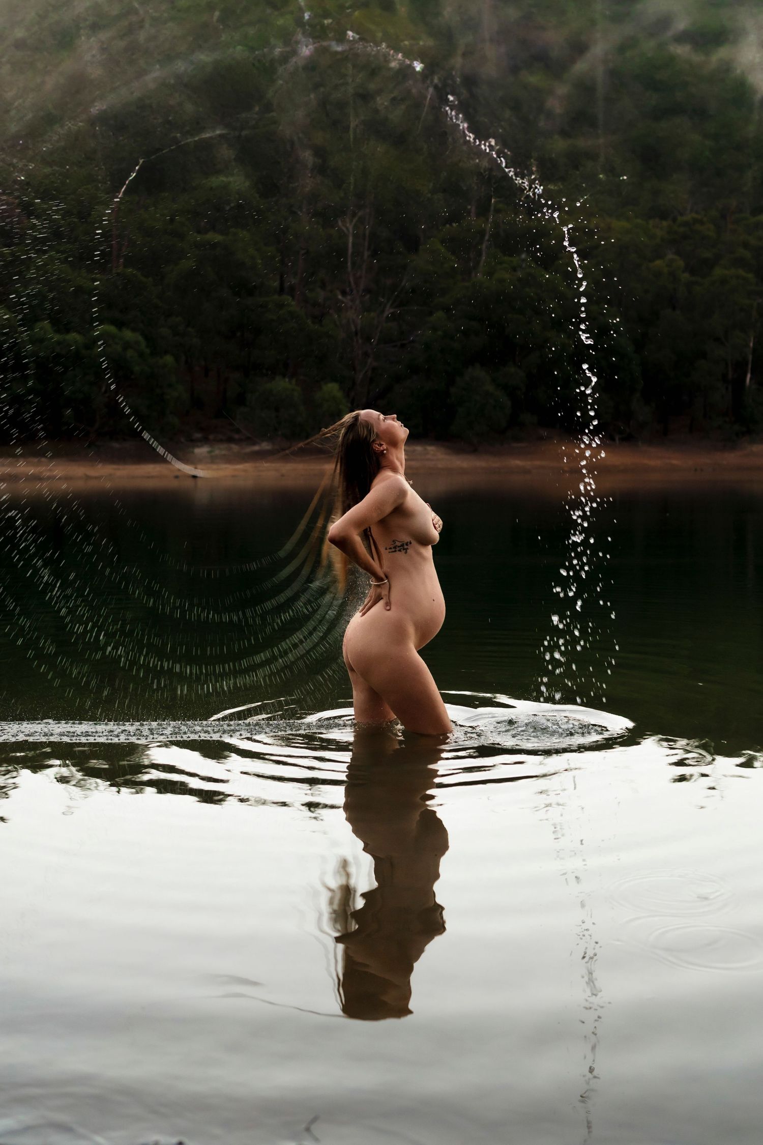 Figure creating graceful water arcs while standing in a serene lake against forested backdrop.