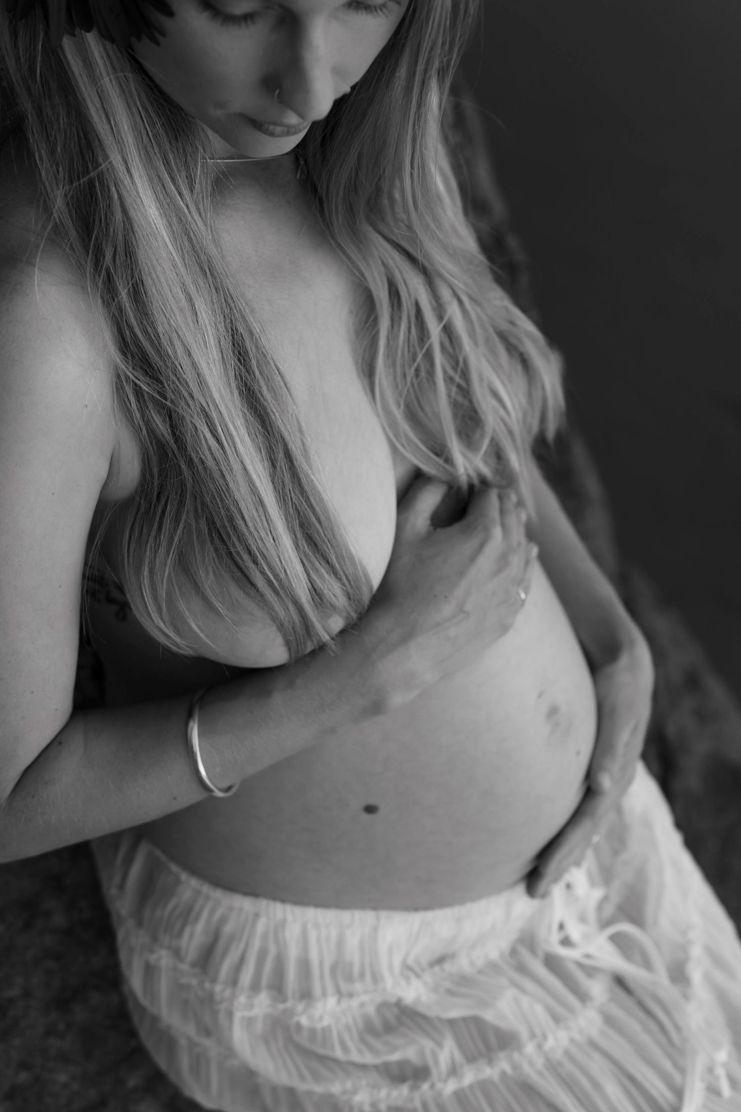 Black and white portrait of pregnant woman in white lace dress touching her belly.