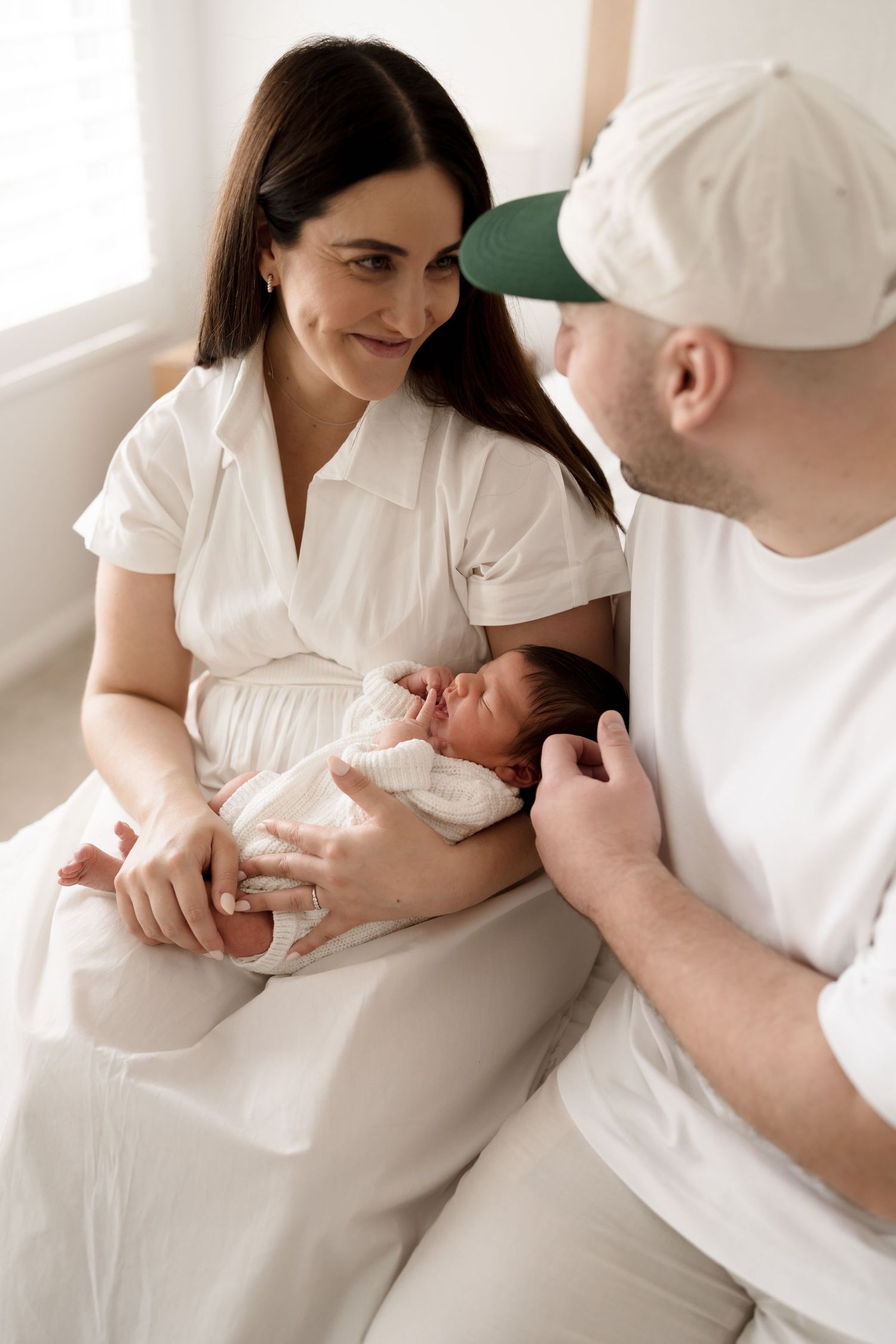 Intimate family photo of parents in white attire sharing a special moment with their newborn child. Meg Rose Photos Perth WA.