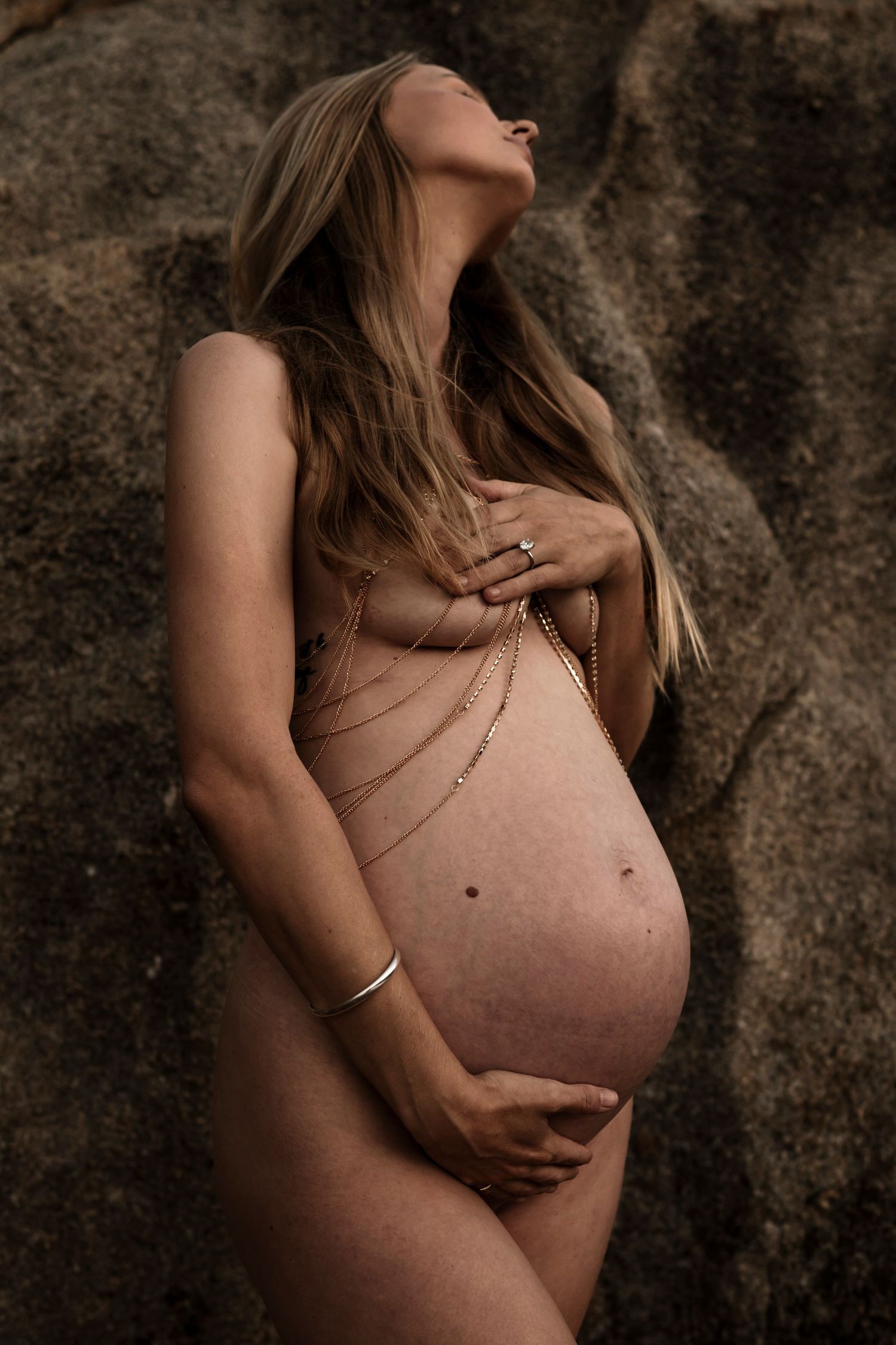 Artistic maternity photo featuring a delicate body chain against natural rock formations.