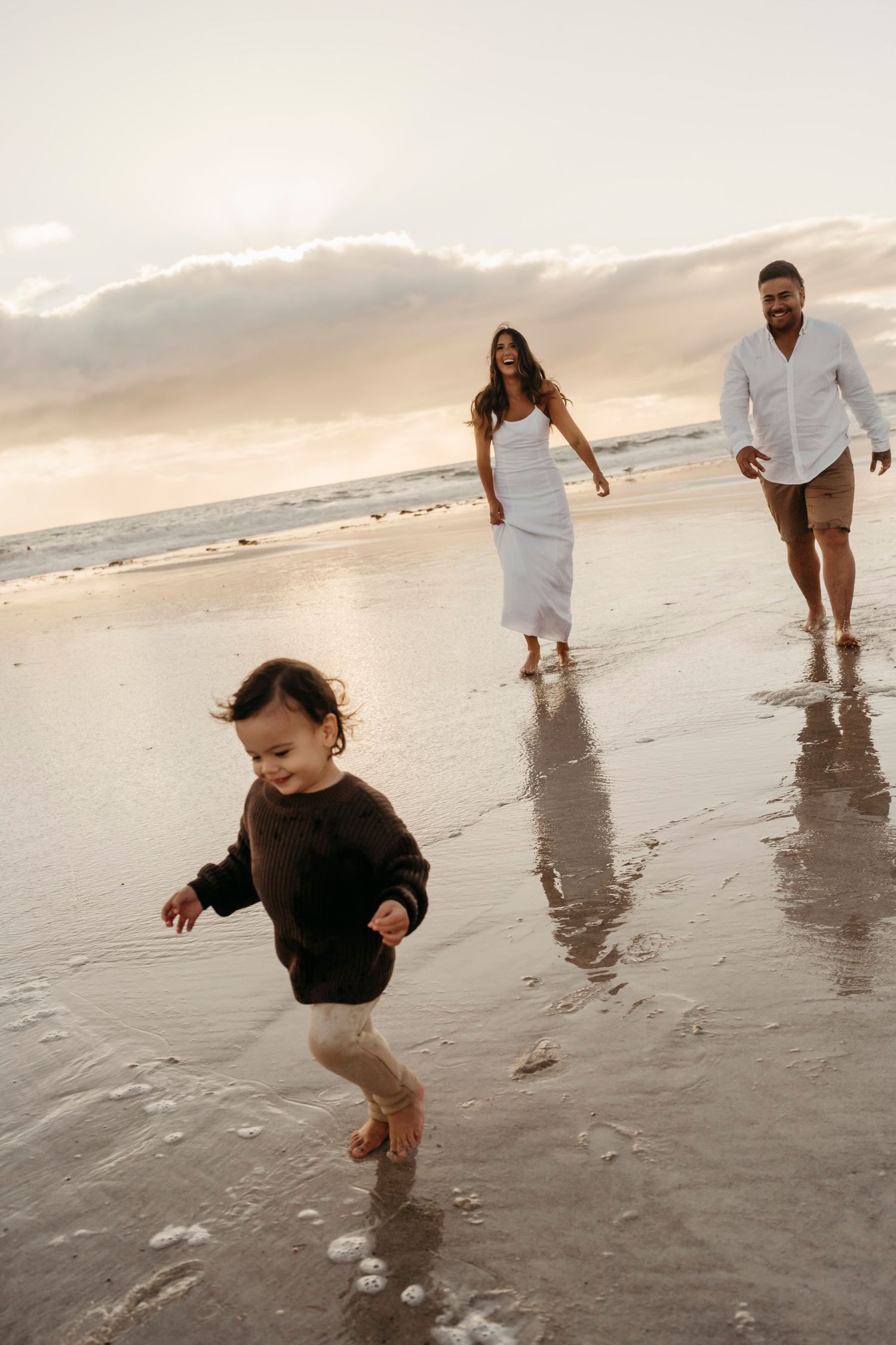 A joyful scene of a family walking and playing together on a cloudy beach at sunset.