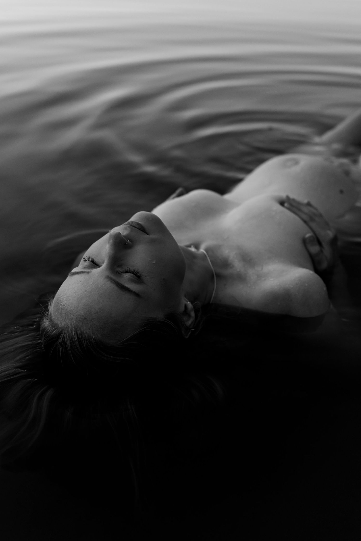 Monochromatic portrait of a person floating serenely in dark water.