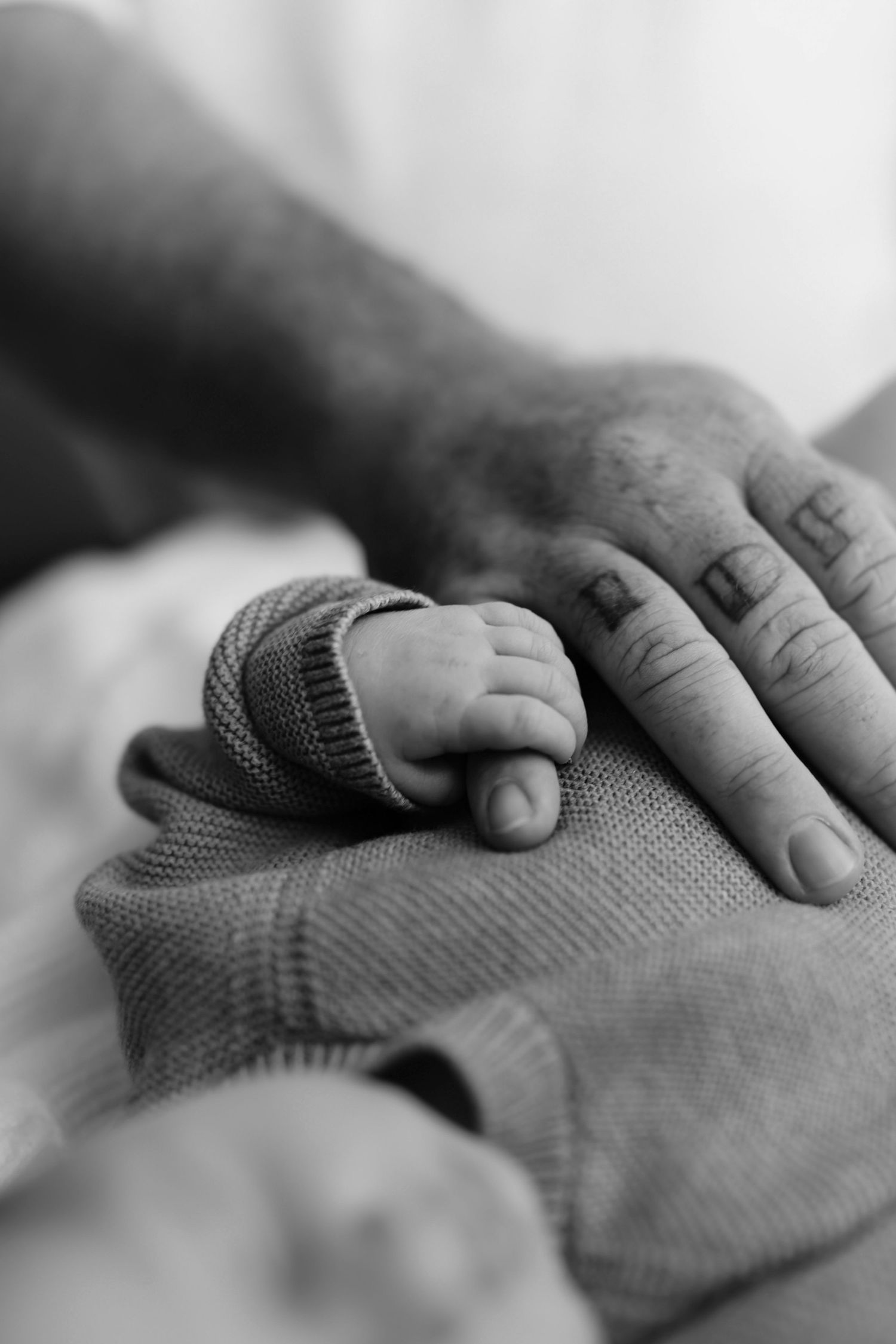 Black and white photo of a newborn baby's tiny hand resting on an adult's larger hand.