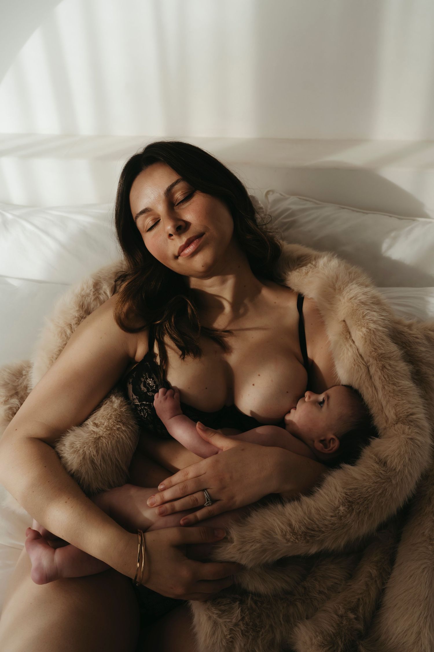 Tender moment of breastfeeding while resting in a cozy fur blanket in soft natural lighting.