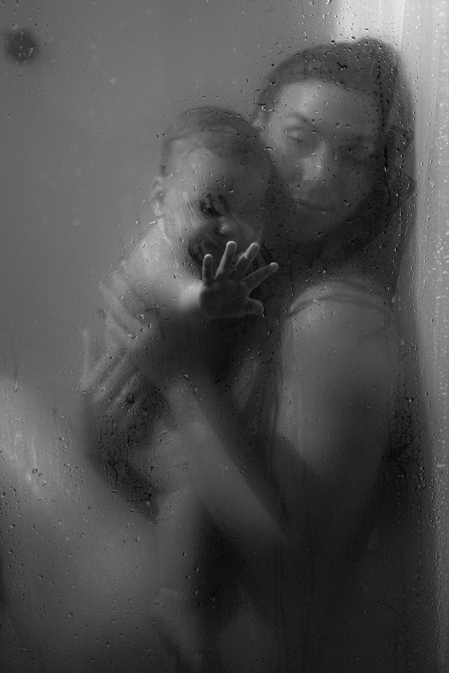 Black and white photo of mother and child behind wet glass, creating a dreamy, intimate silhouette effect.