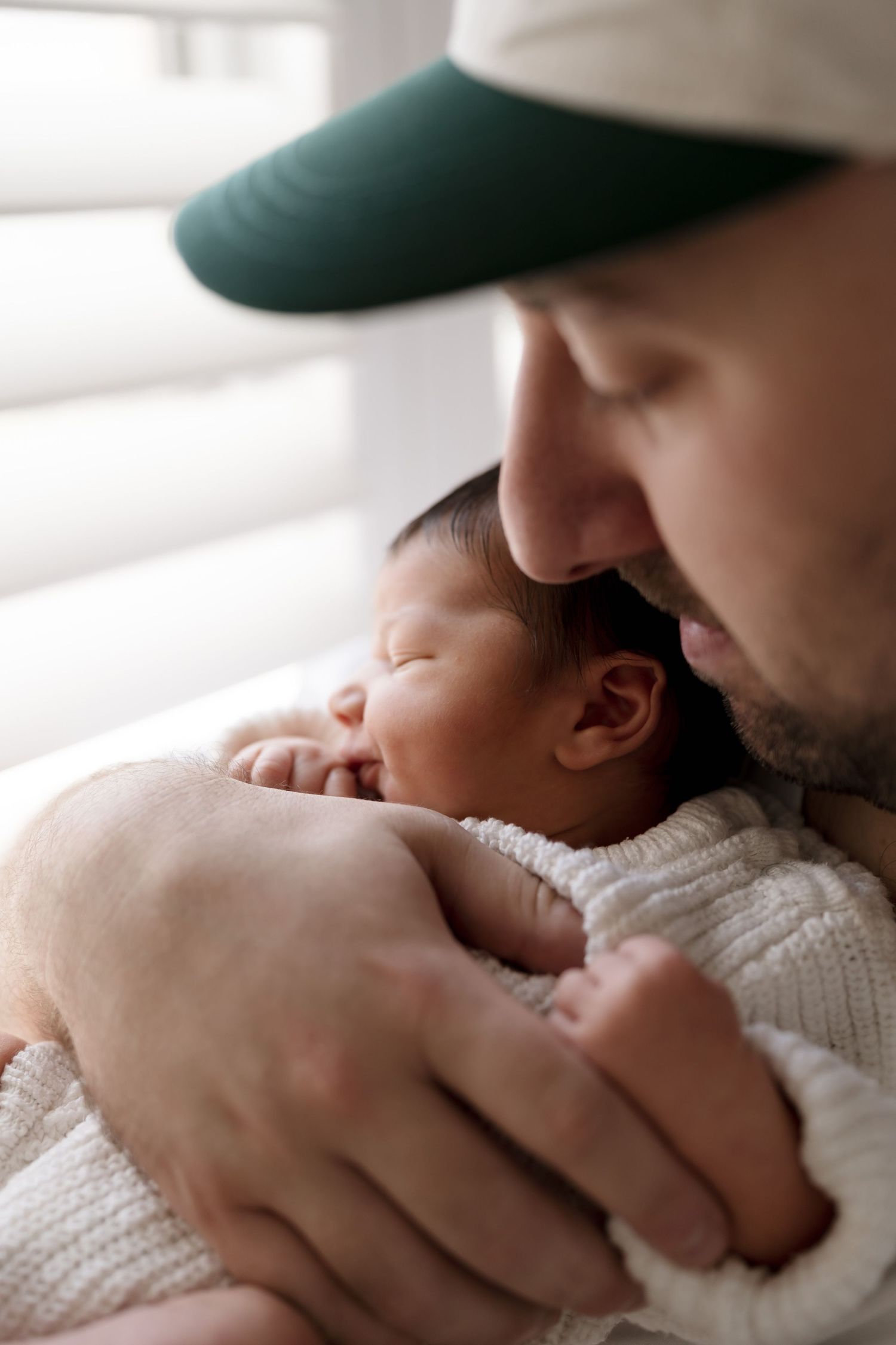 A tender moment captured in natural light as a nurturing parent cradles a sleeping newborn baby in a white knit blanket.