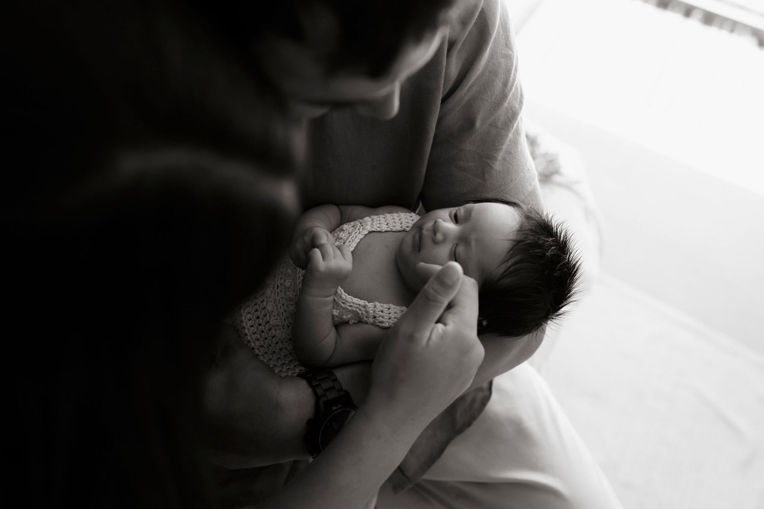 Black and white photo of a parent cradling a sleeping newborn baby in their arms.