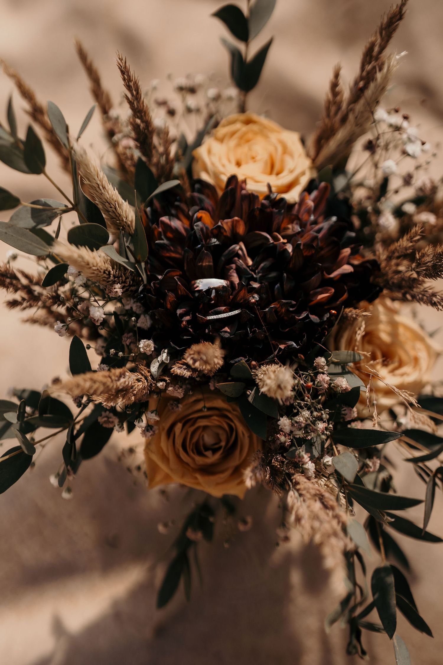 Moody wedding bouquet featuring peach roses, dark pinecones, and dried elements in vintage style.
