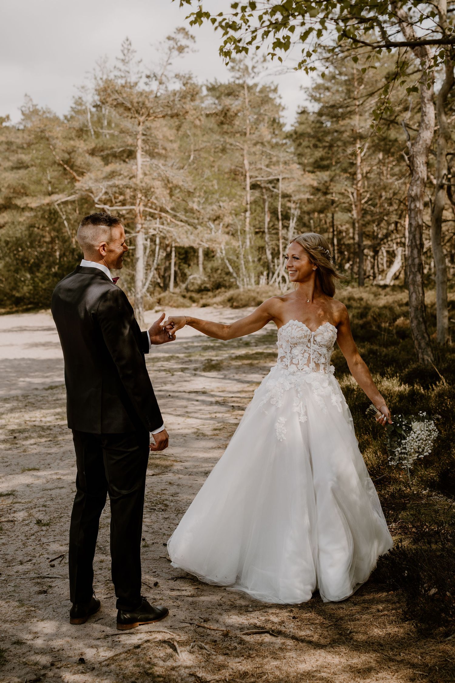 A couple in wedding attire share a romantic moment dancing together in a scenic forest setting.