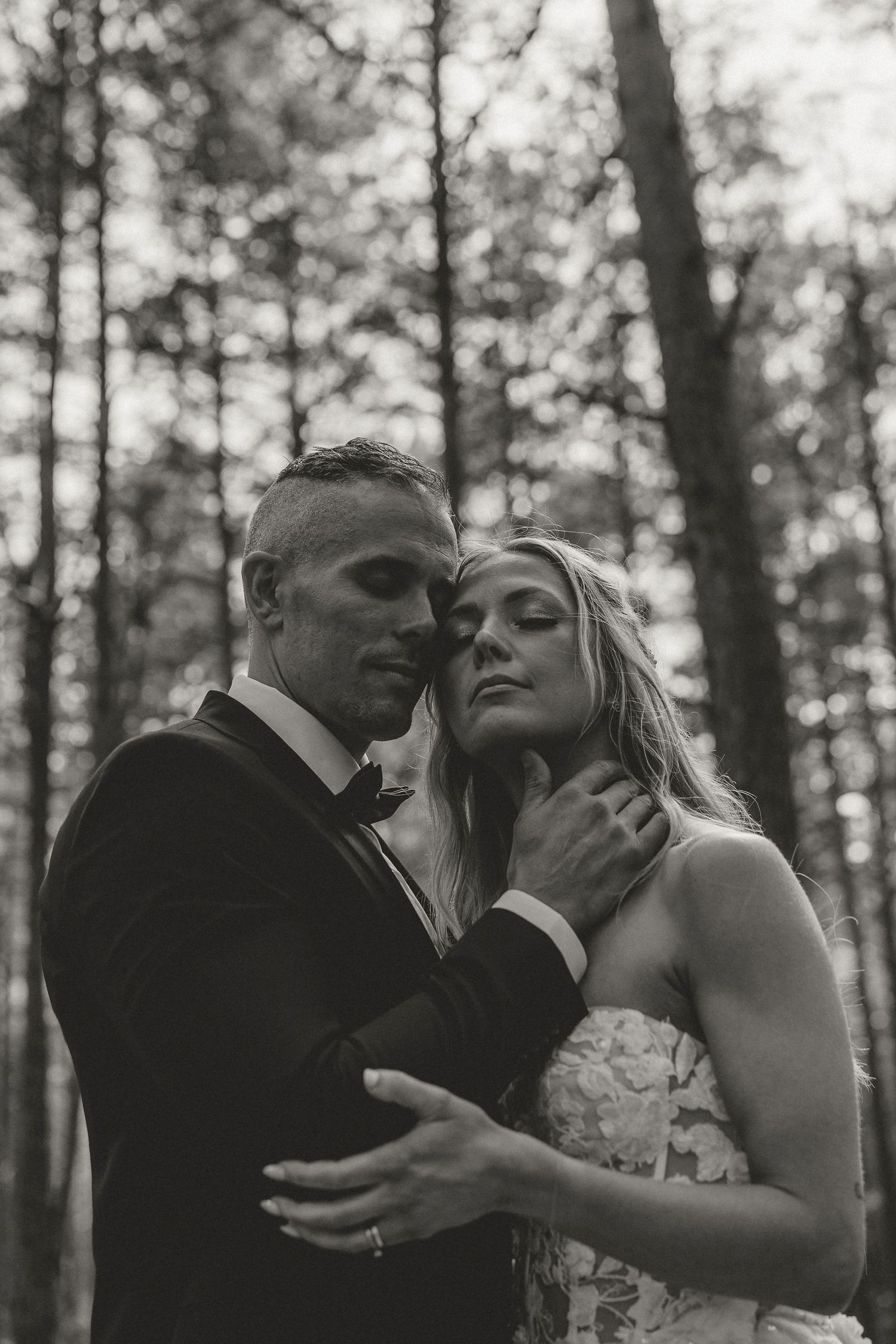 Black and white romantic wedding photo of newlyweds embracing intimately in a misty forest setting.