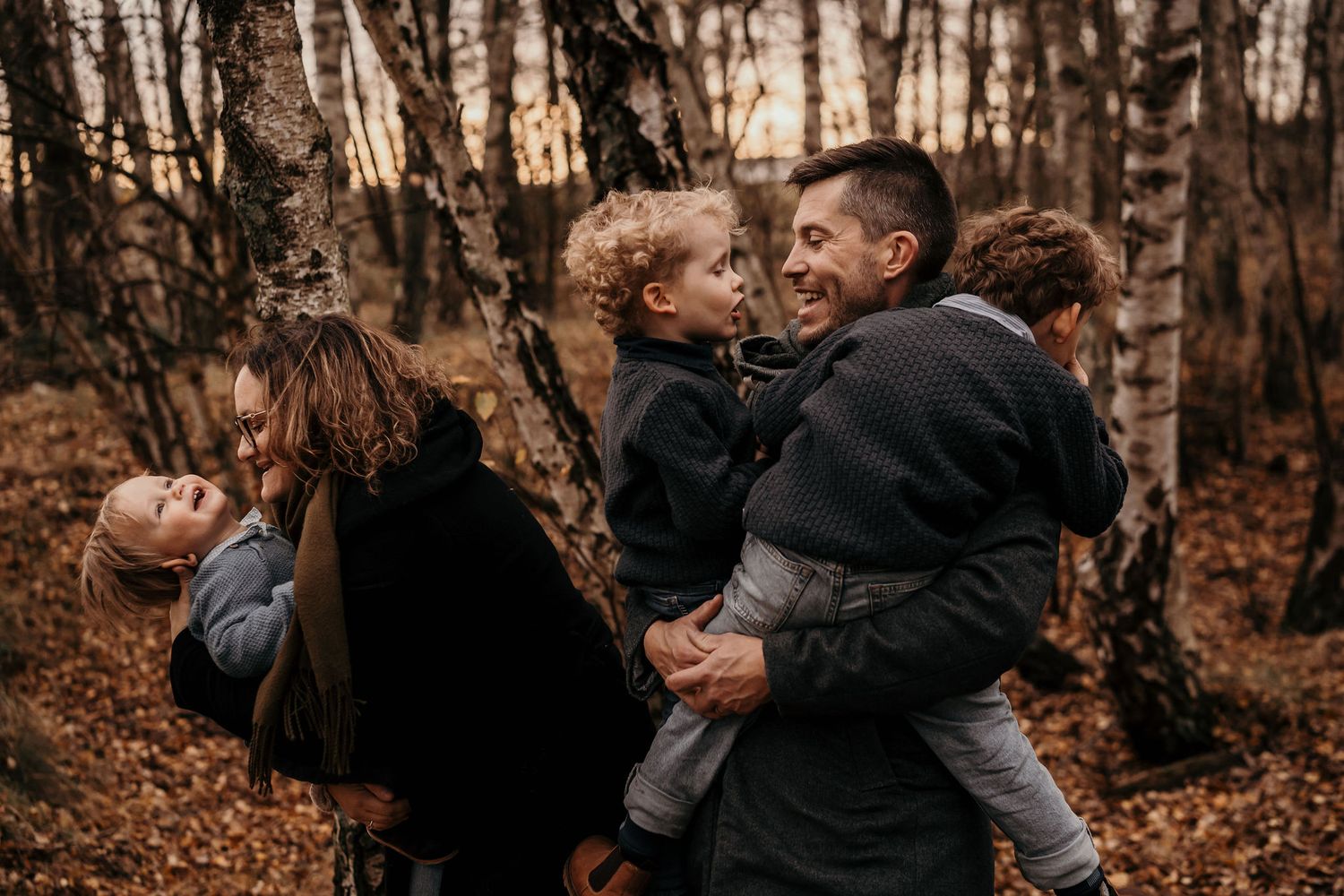 A tender family moment captured in a forest with warm autumn colors and golden light filtering through trees.