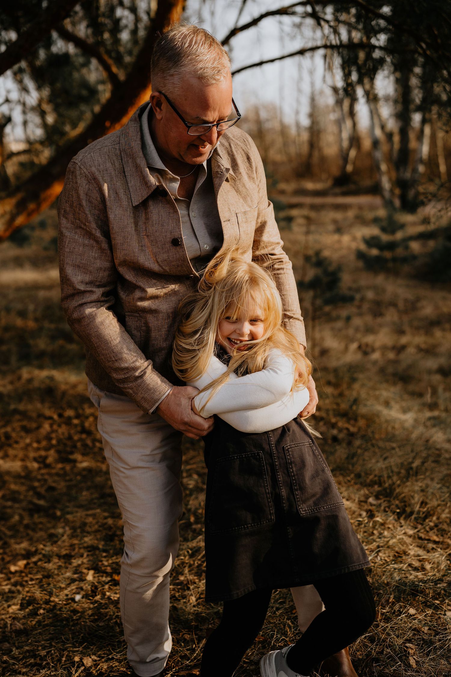 A warm autumn scene shows a tender moment between adult and child embracing outdoors in golden sunlight.
