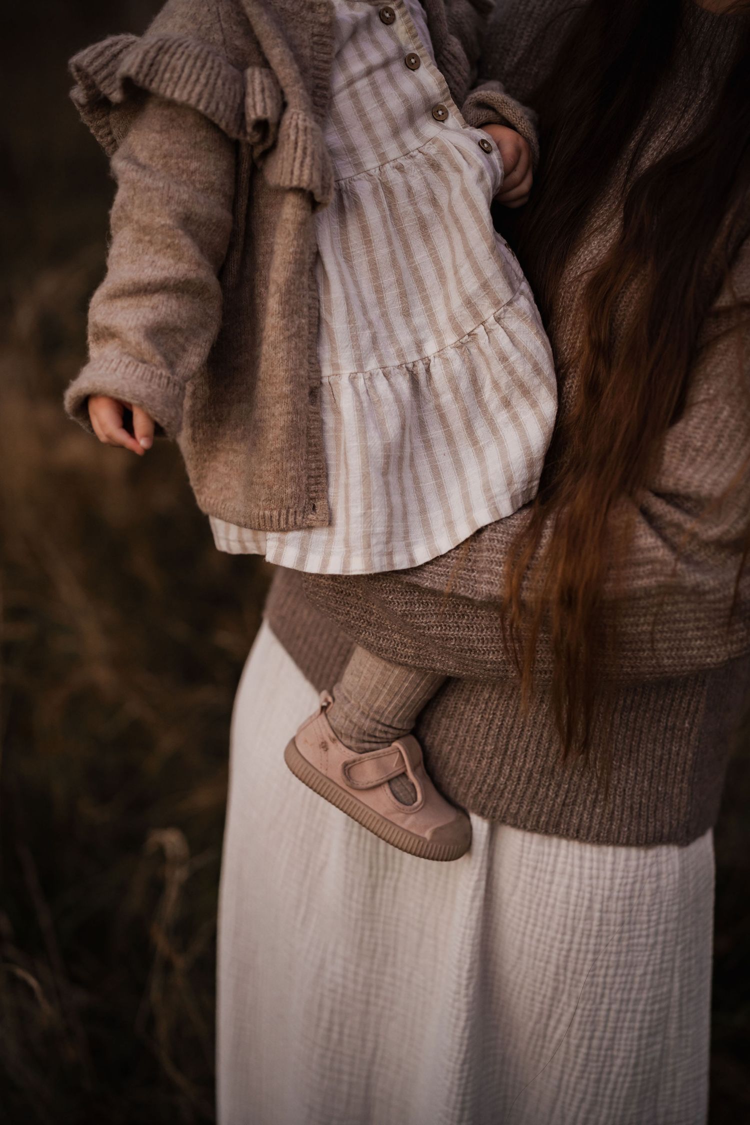 Close-up detail of brown knit sweater and white dress with small shoes.