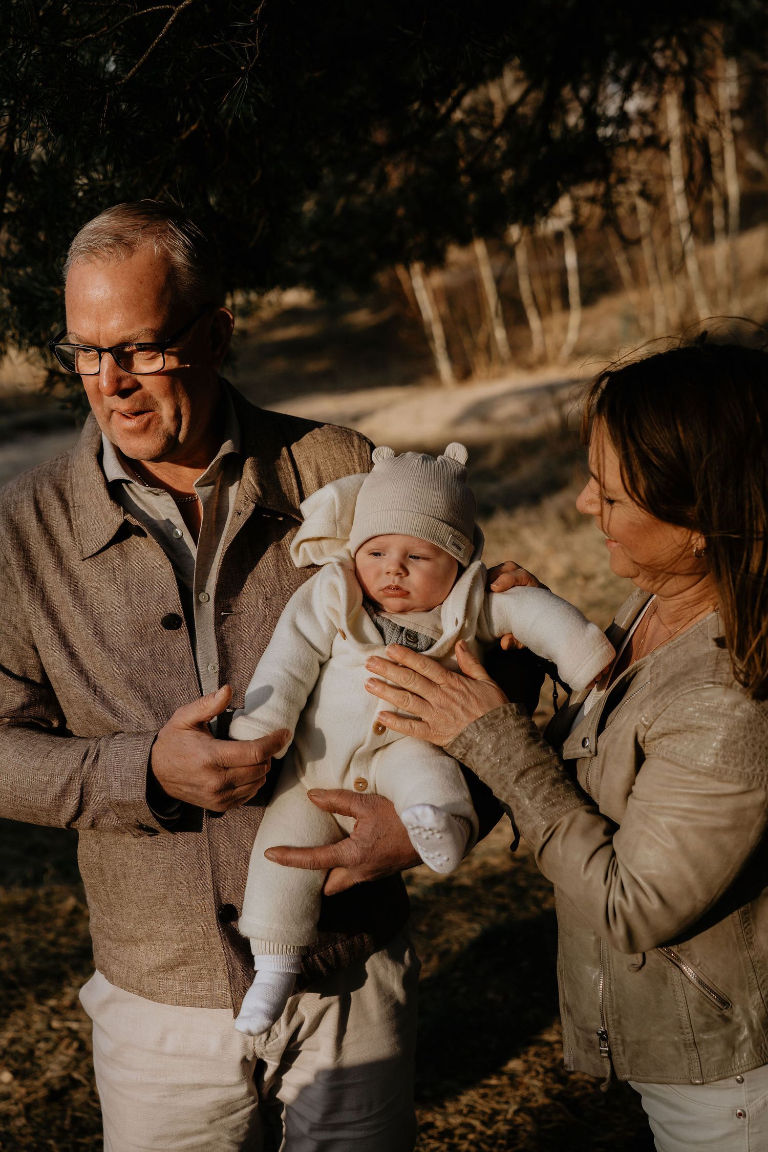 Family sharing a tender moment together with their baby outdoors during golden hour in an autumn setting.