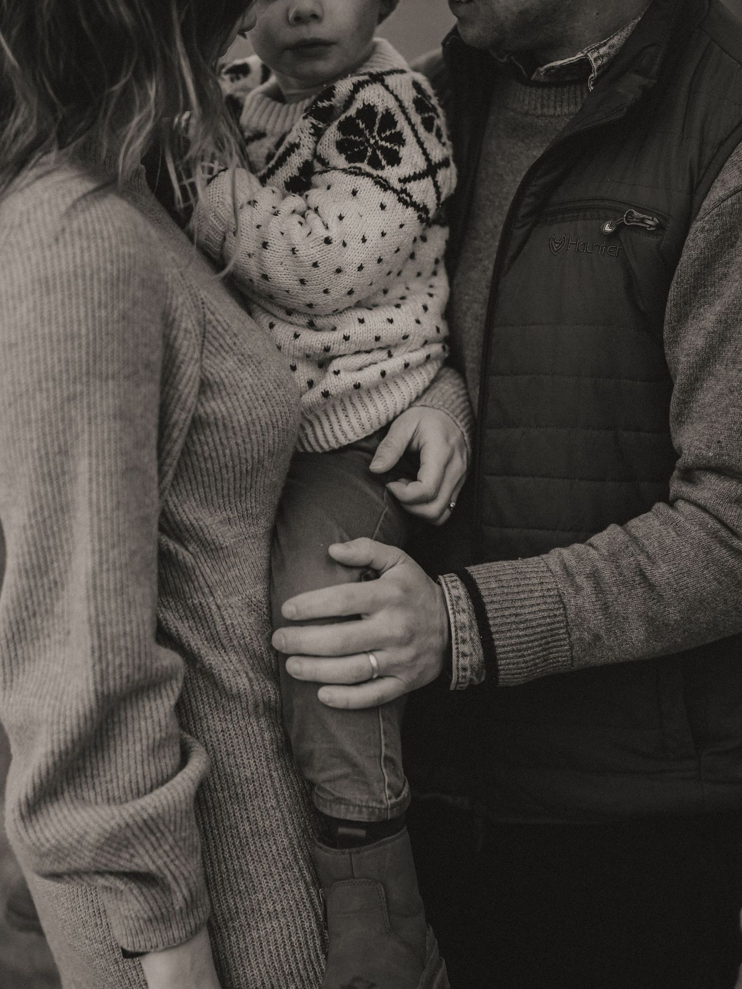 Black and white close-up of family members wearing cozy sweaters embracing together.