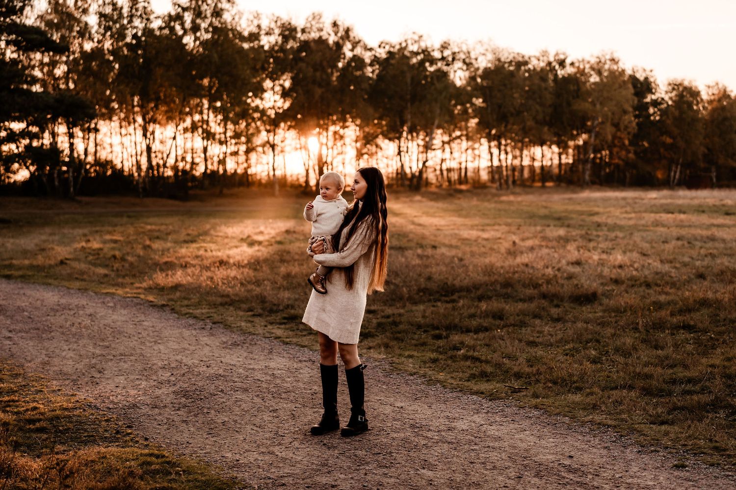 A silhouetted figure stands on a path at sunset with tall trees in the background.