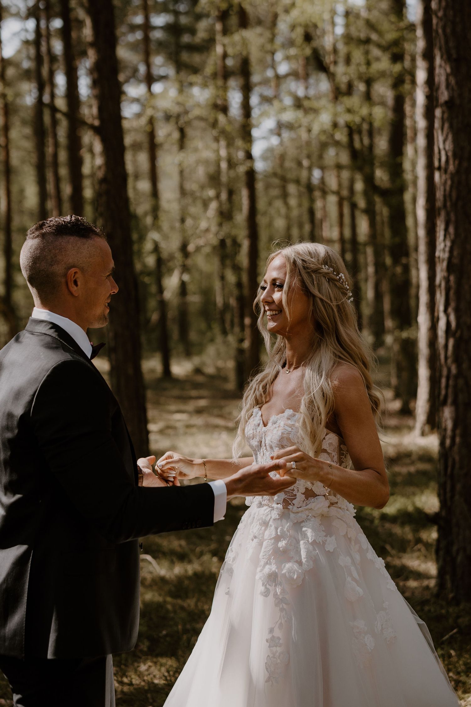 A couple shares an intimate moment during their wedding ceremony in a sunlit pine forest.