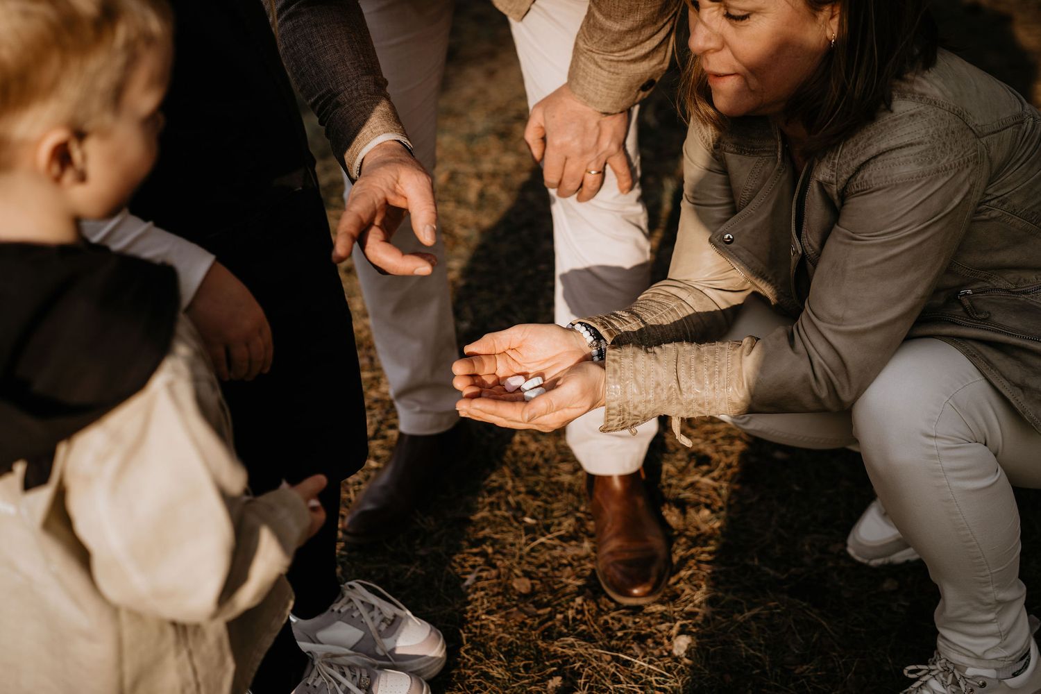 People sit together outdoors on mulch ground examining something in their hands during outdoor gathering.