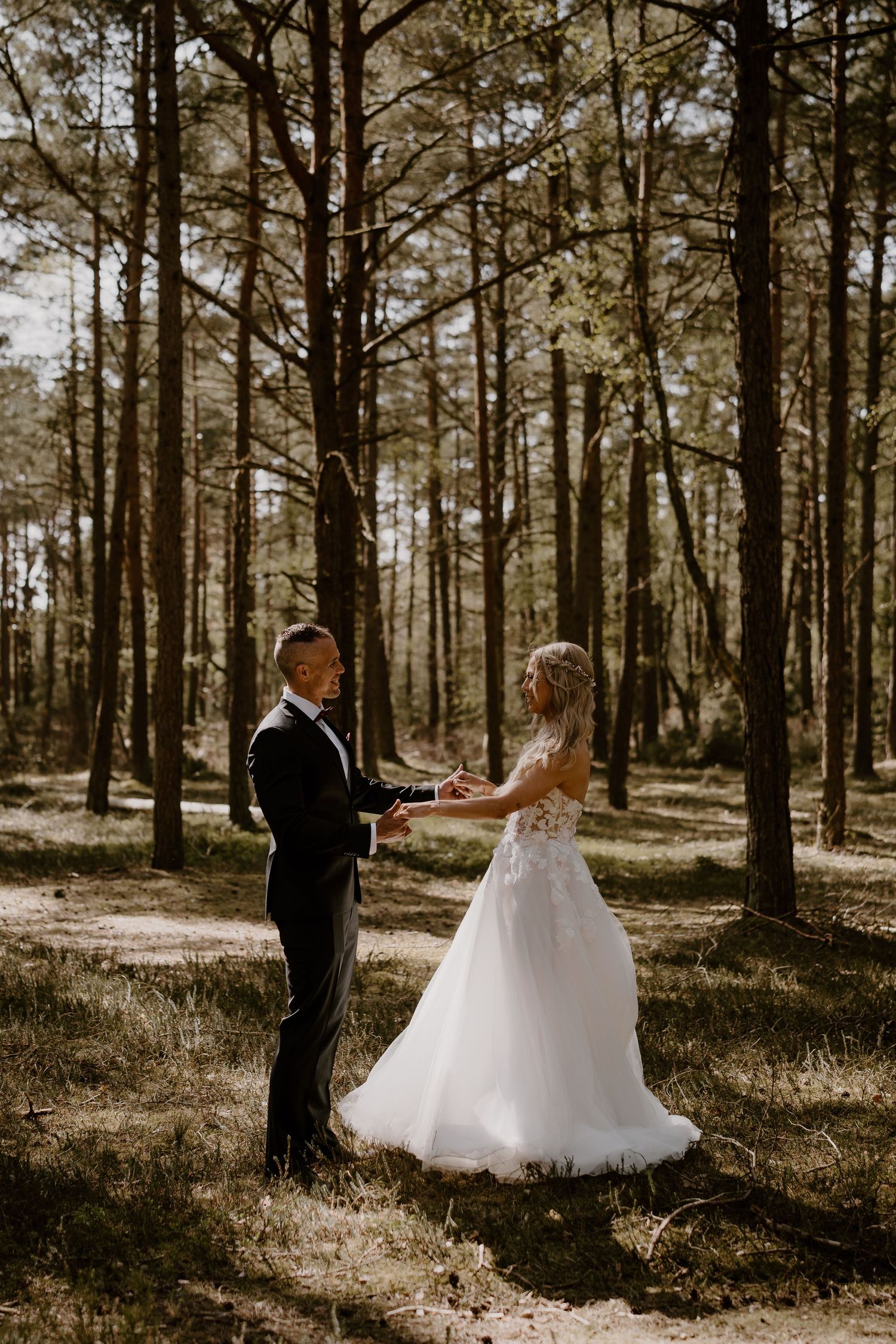 A couple in wedding attire exchange vows in a sunlit pine forest during an intimate outdoor ceremony.