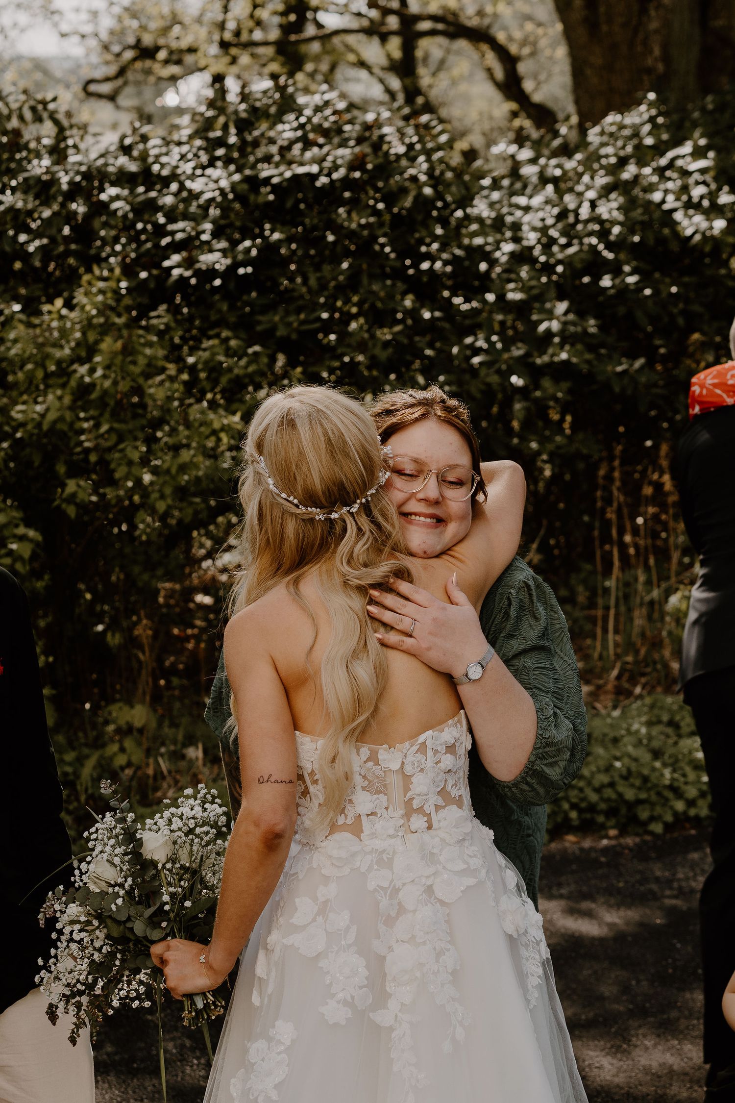 An emotional bridal moment captured outdoors with white floral blossoms and blooming trees in the background.