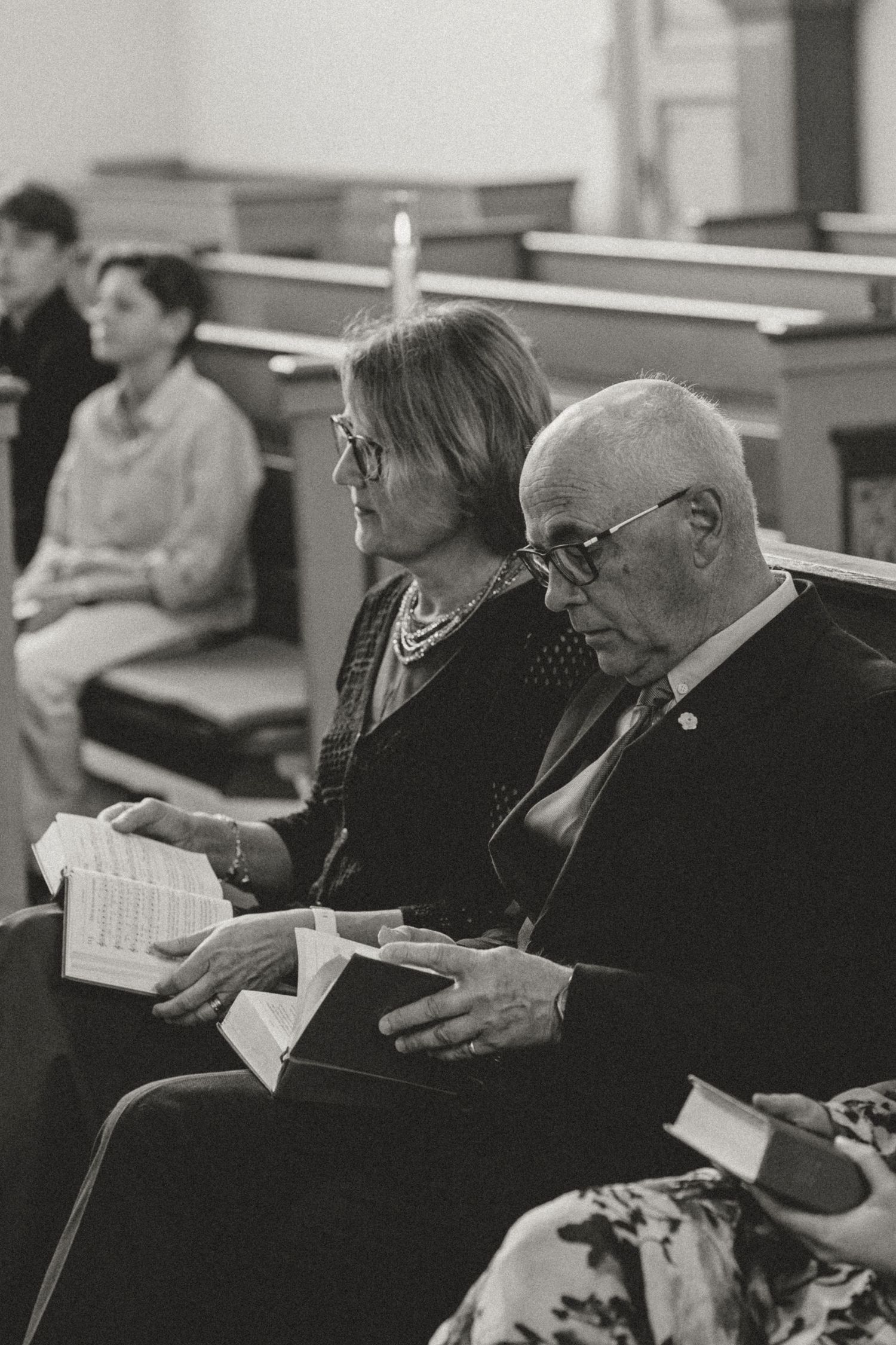 Black and white photo of people sitting in church pews reading from books during a service or gathering.