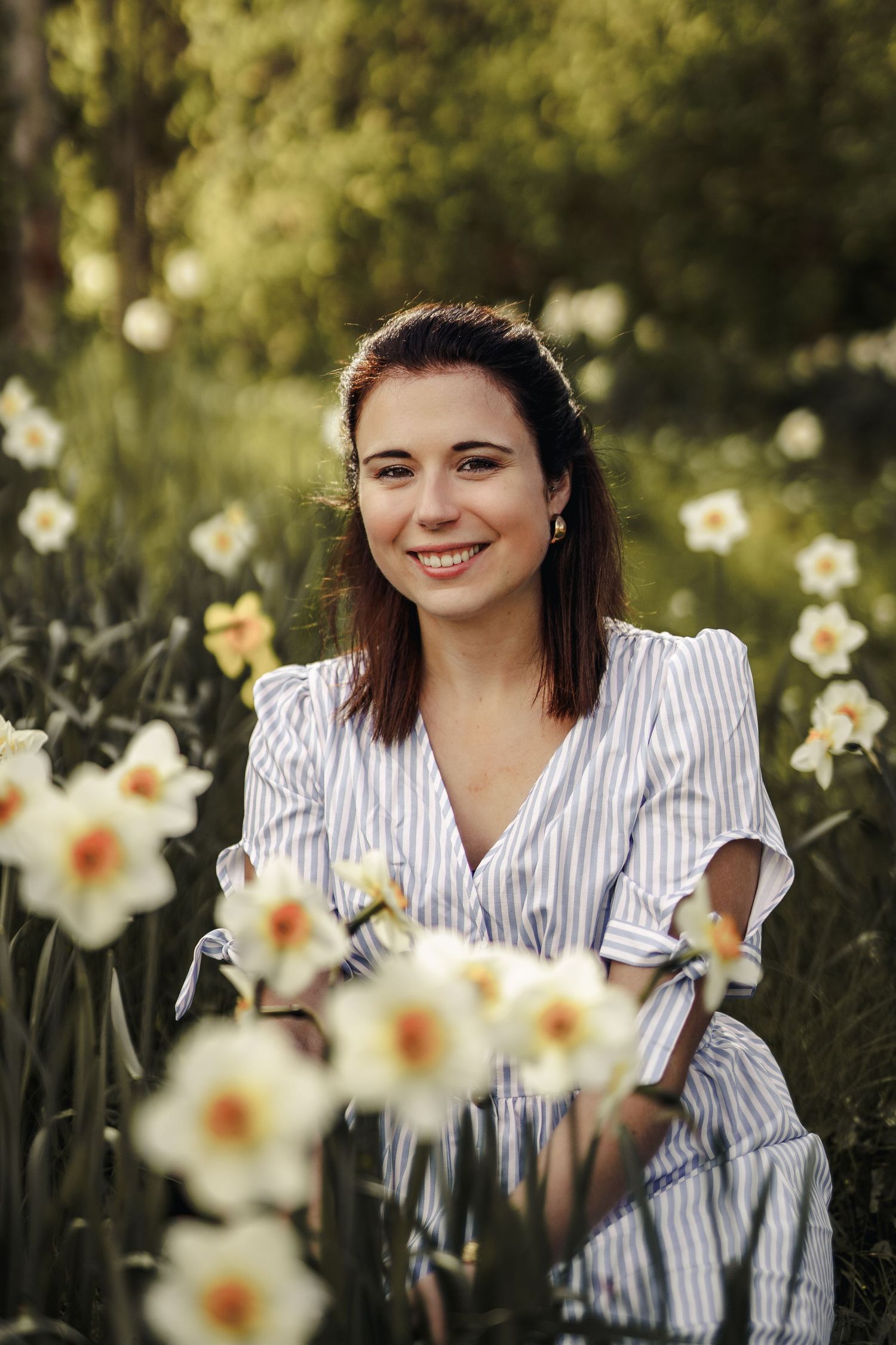 Portrait in a blooming daffodil garden with someone wearing a white striped blouse on a sunny spring day.