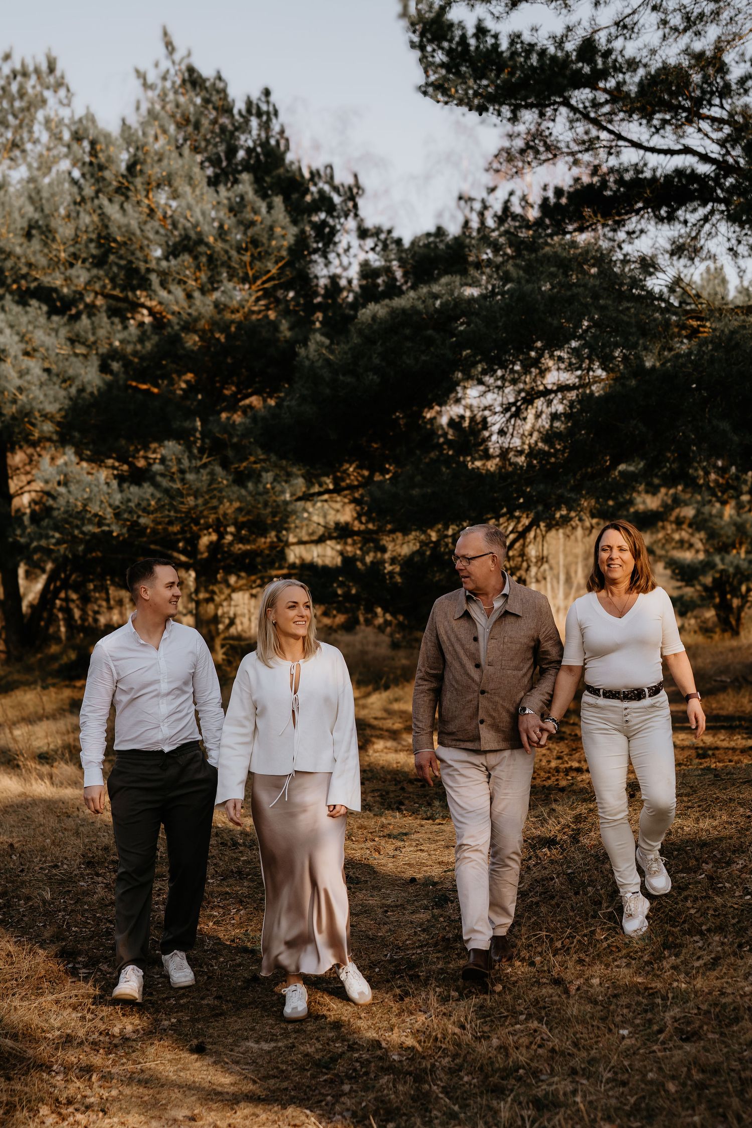 A group walks together on a nature path during golden hour wearing casual outfits in neutral colors.