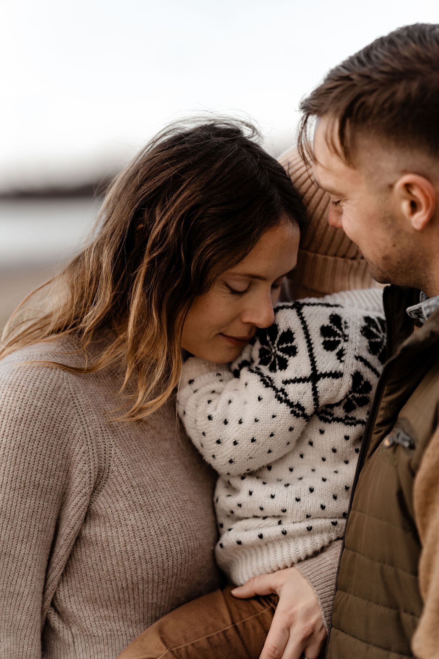 Intimate family moment captured in soft neutral tones with knit sweaters and close embraces.