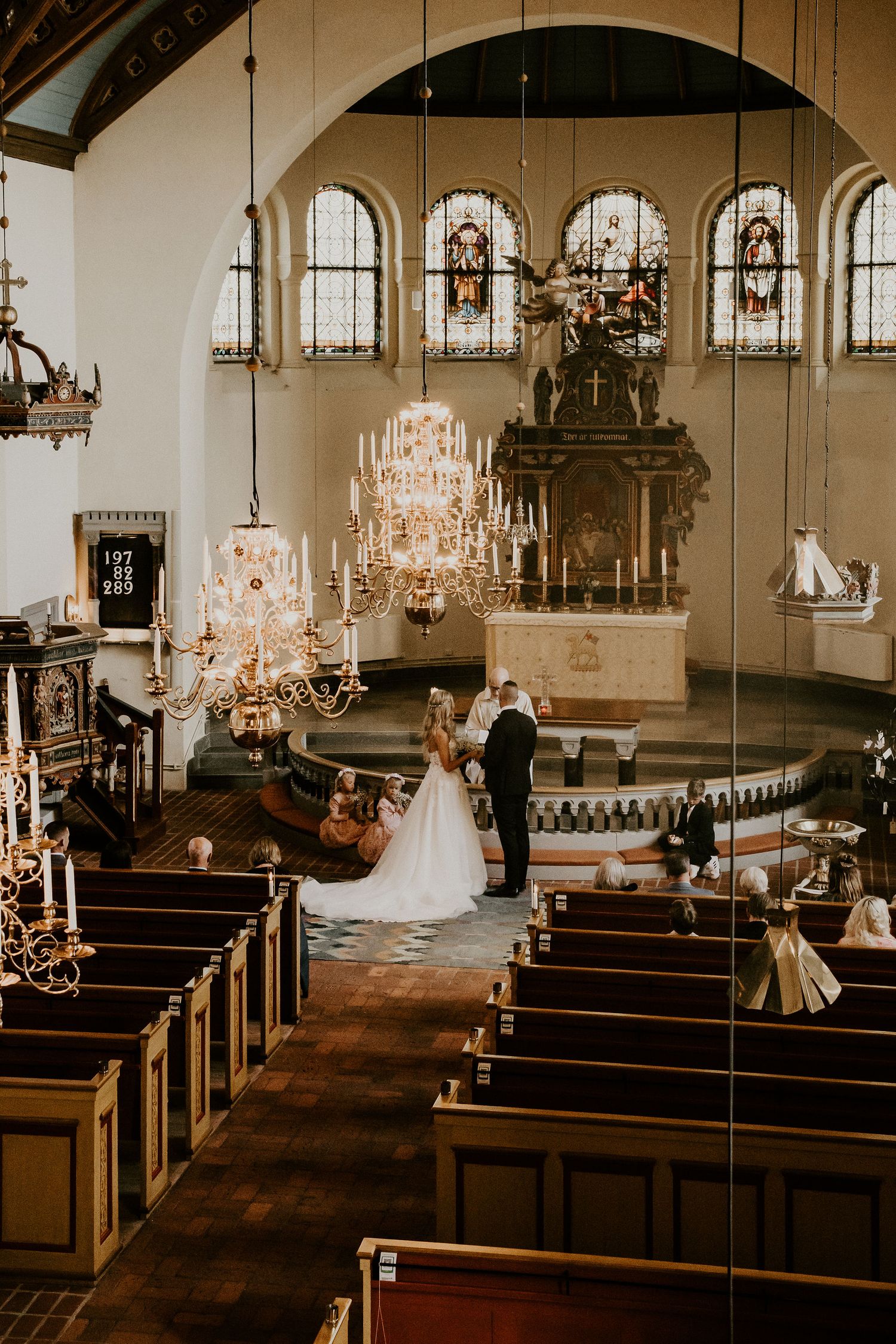 A traditional church wedding ceremony under elegant crystal chandeliers and arched stained glass windows in a historic sanctuary.