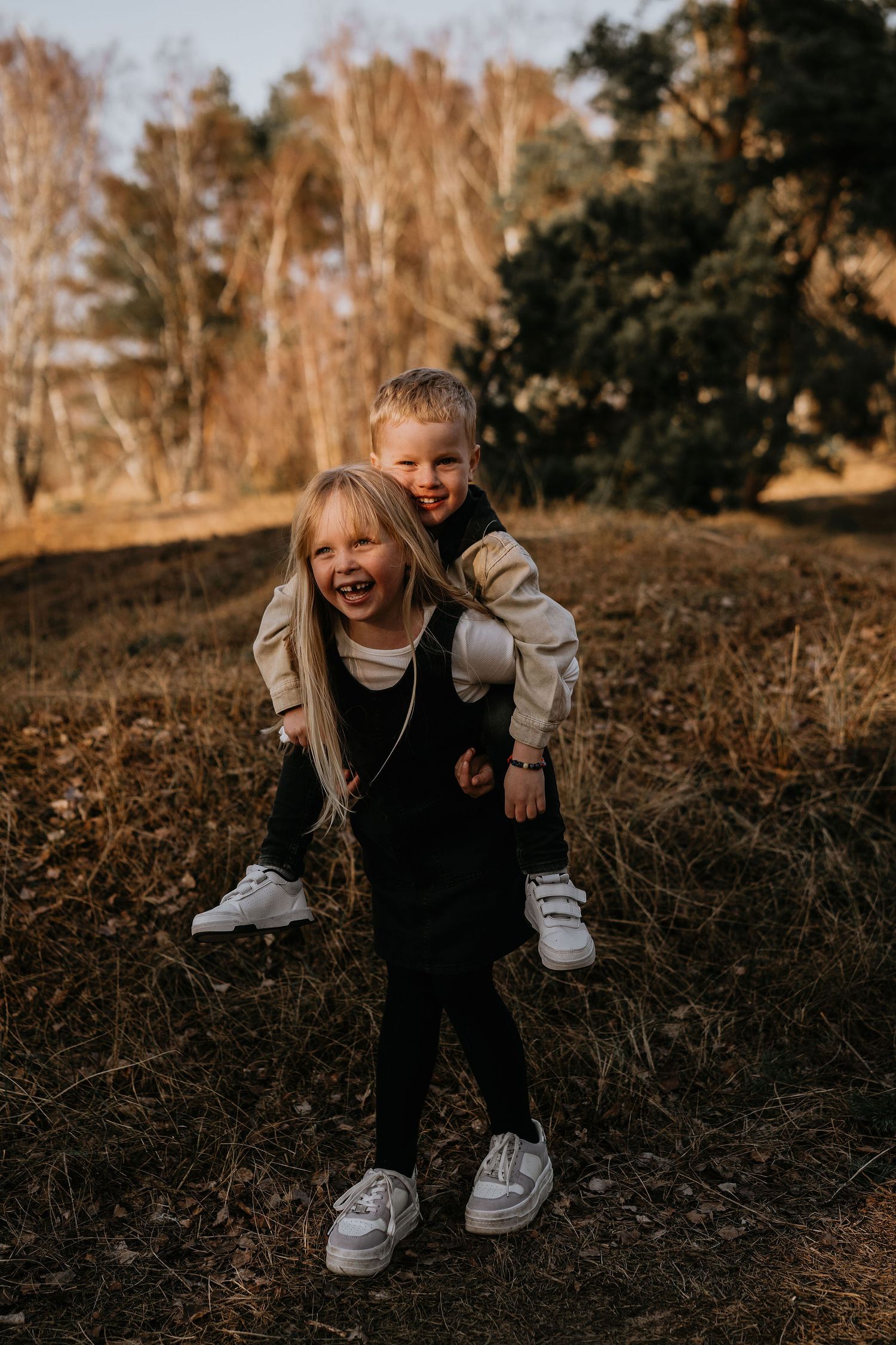 Two young children laughing and playing outdoors in autumn with one giving a piggyback ride to the other.