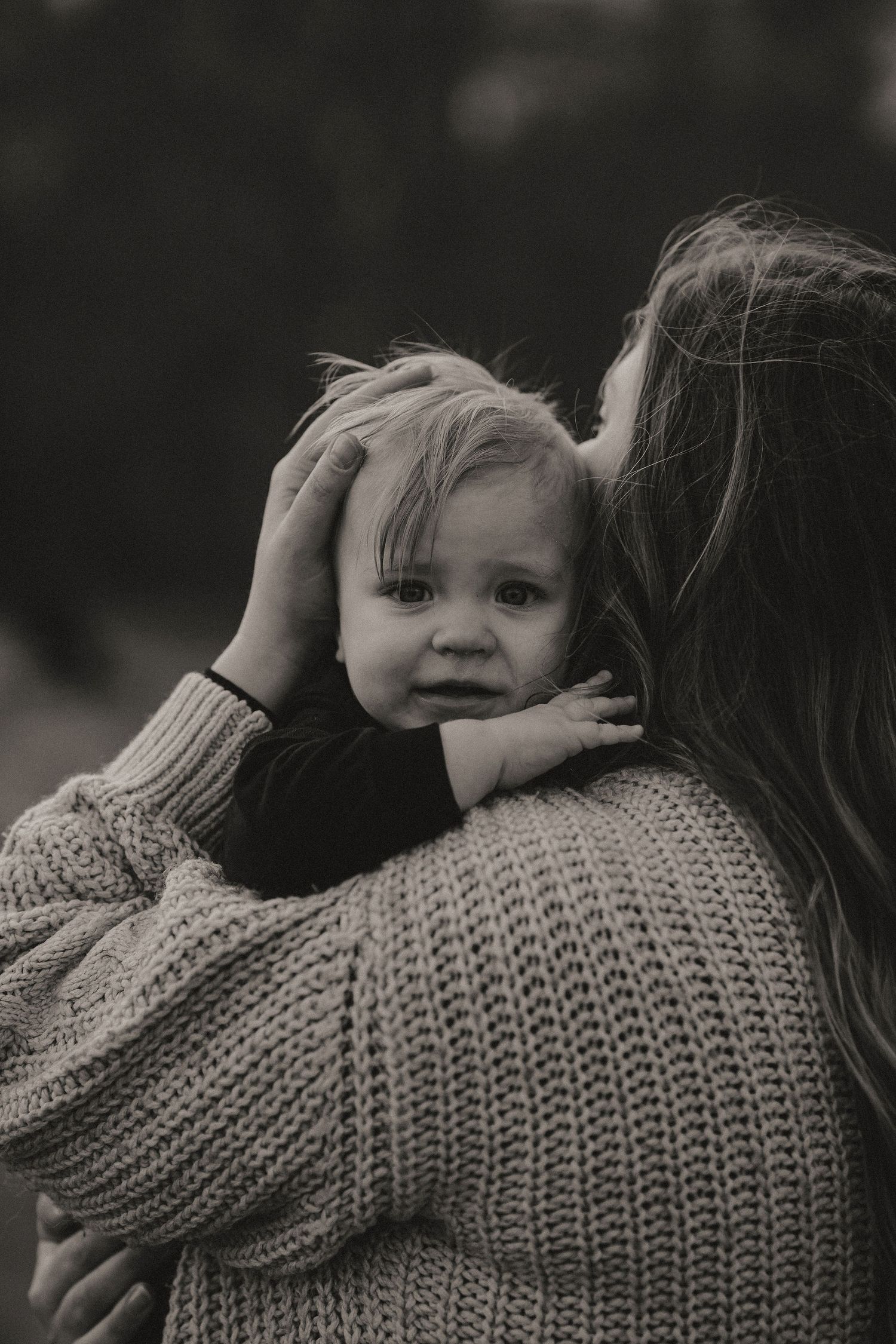 A tender moment captured in black and white as someone holds a small child wearing a knit sweater.