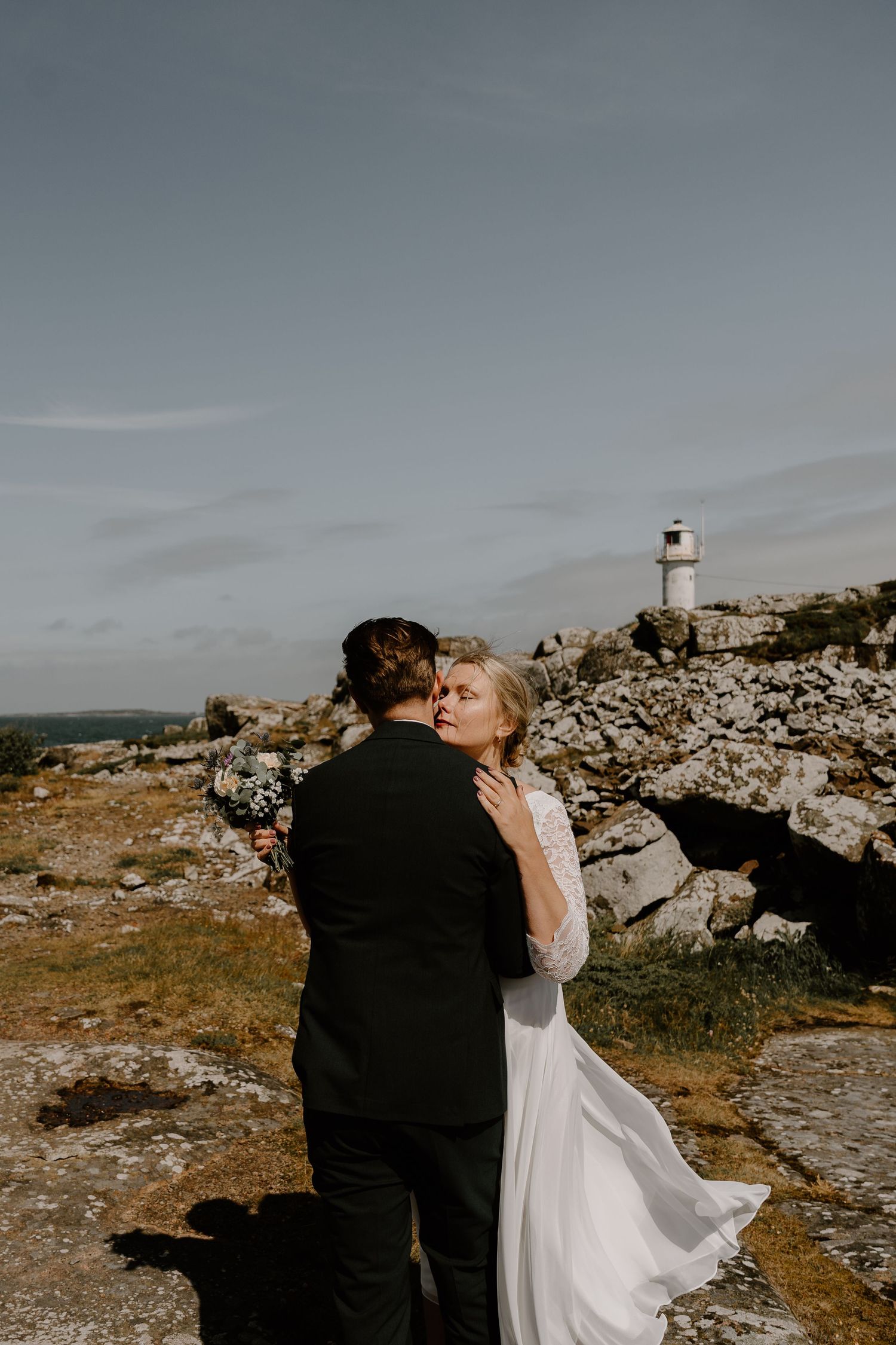 A romantic couple shares intimate moments on a mountainous landscape with rocky outcrops under an overcast sky.
