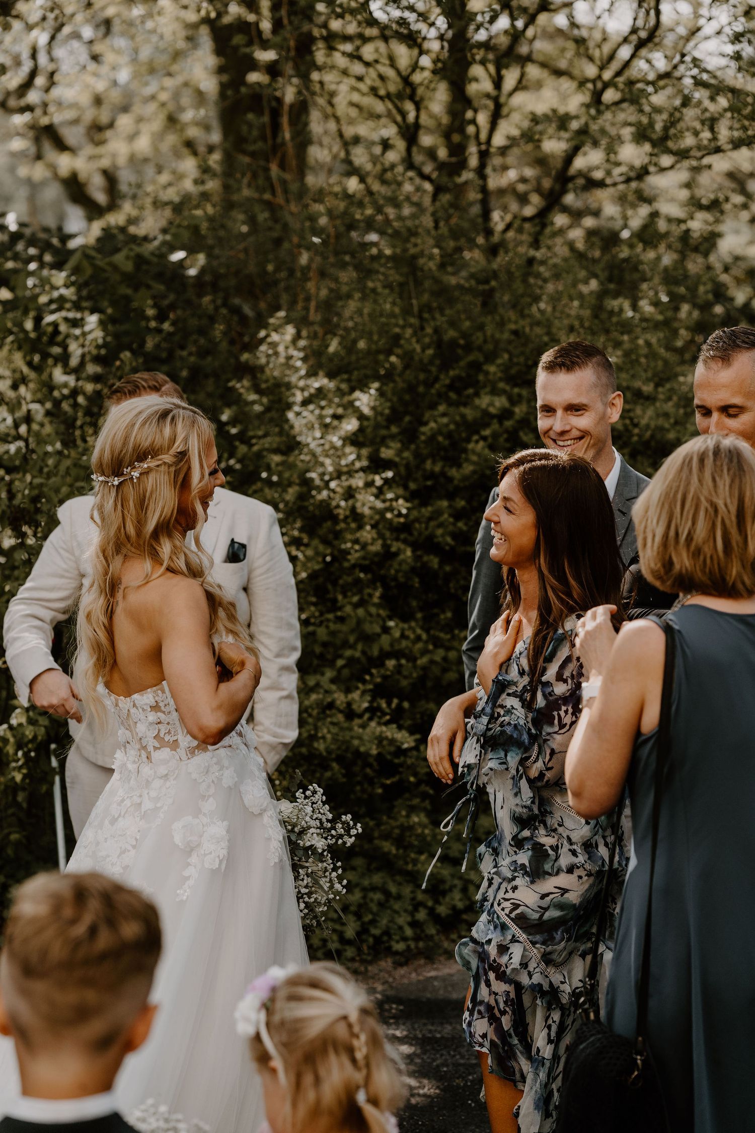 A wedding moment outdoors with guests sharing laughter in a natural wooded setting at golden hour.