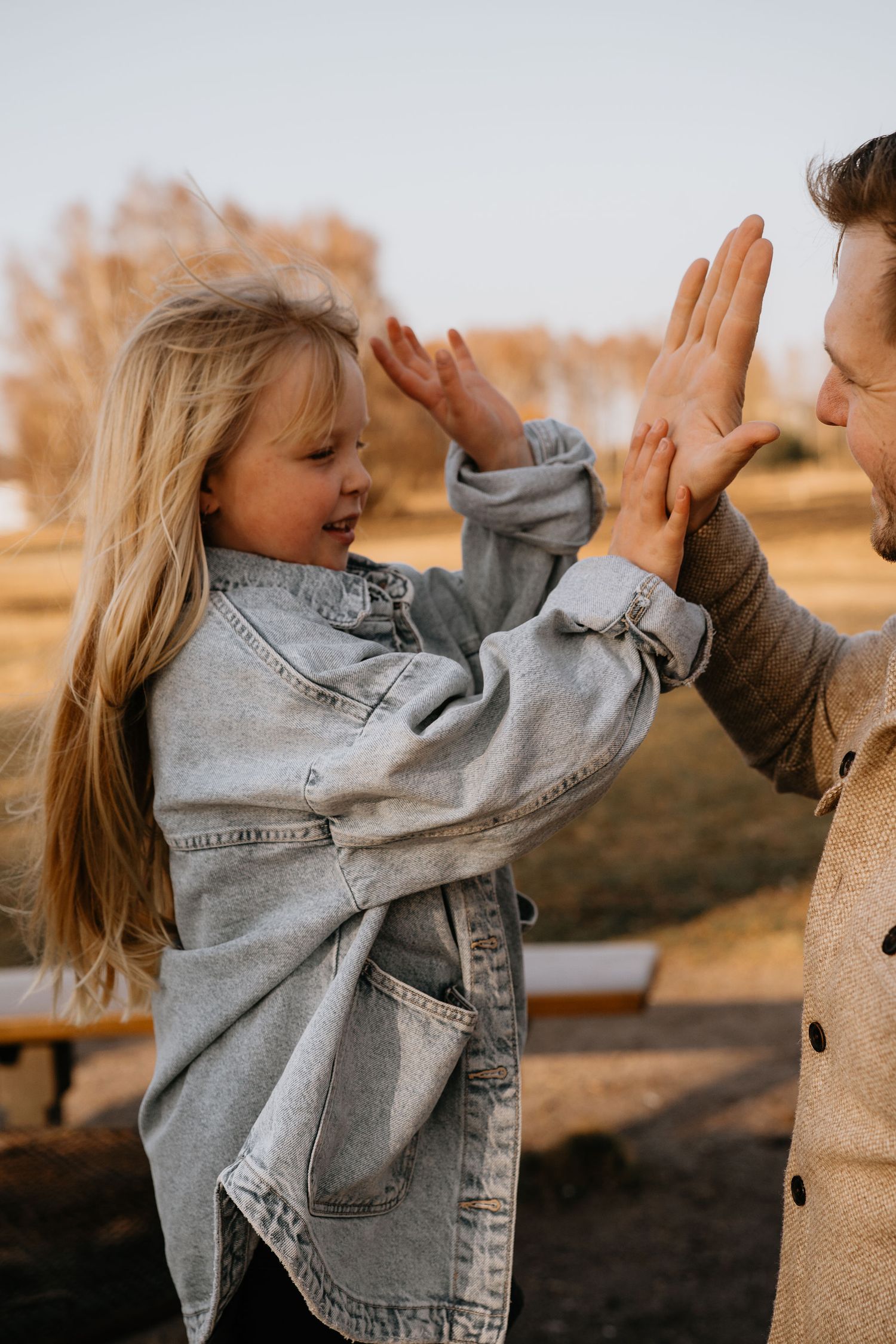 Two people share a joyful high-five moment outdoors while wearing casual denim and autumn clothing at sunset.
