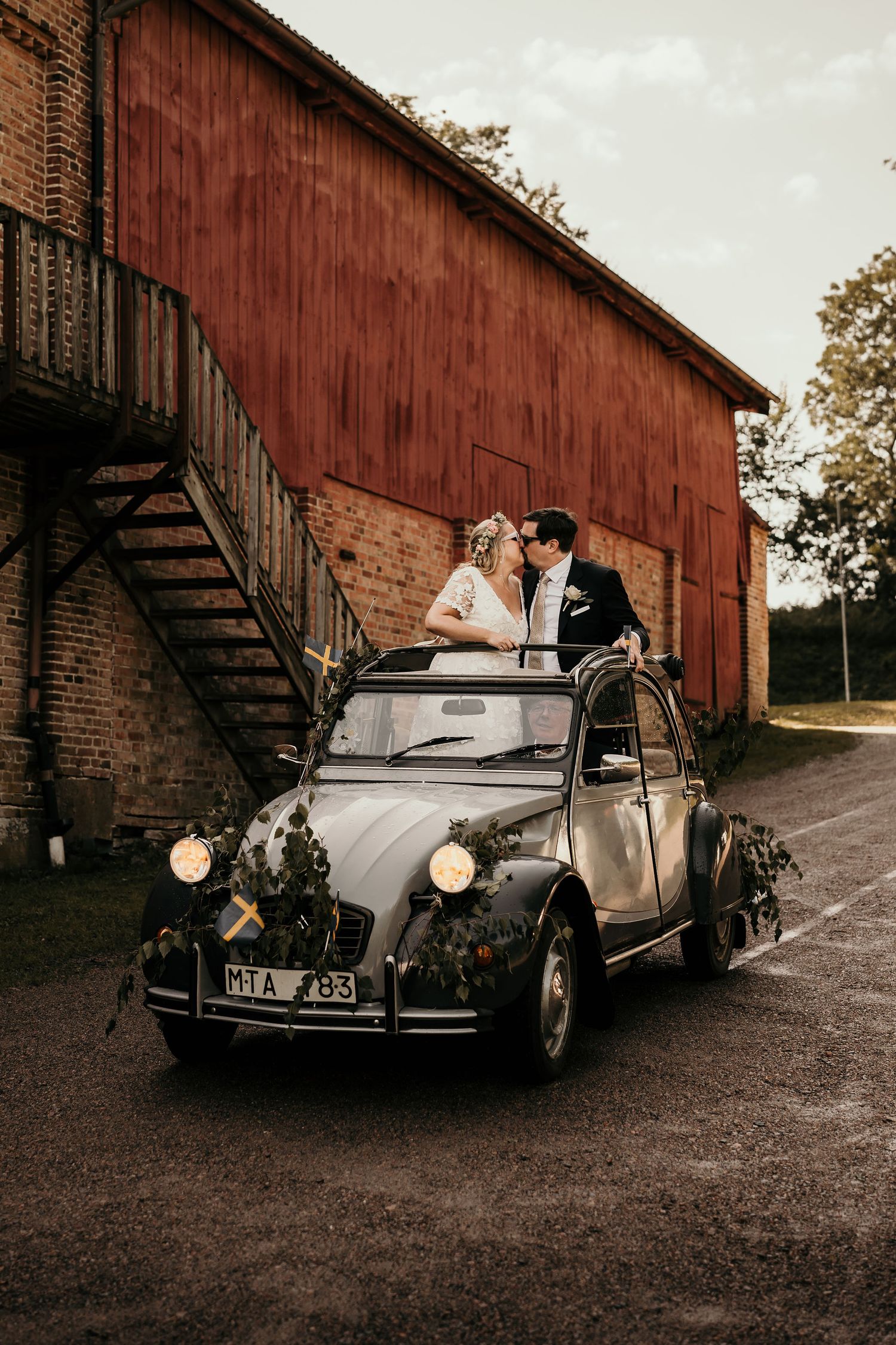 Classic Citroen 2CV car parked in front of rustic red barn with brick details on a cloudy autumn day.
