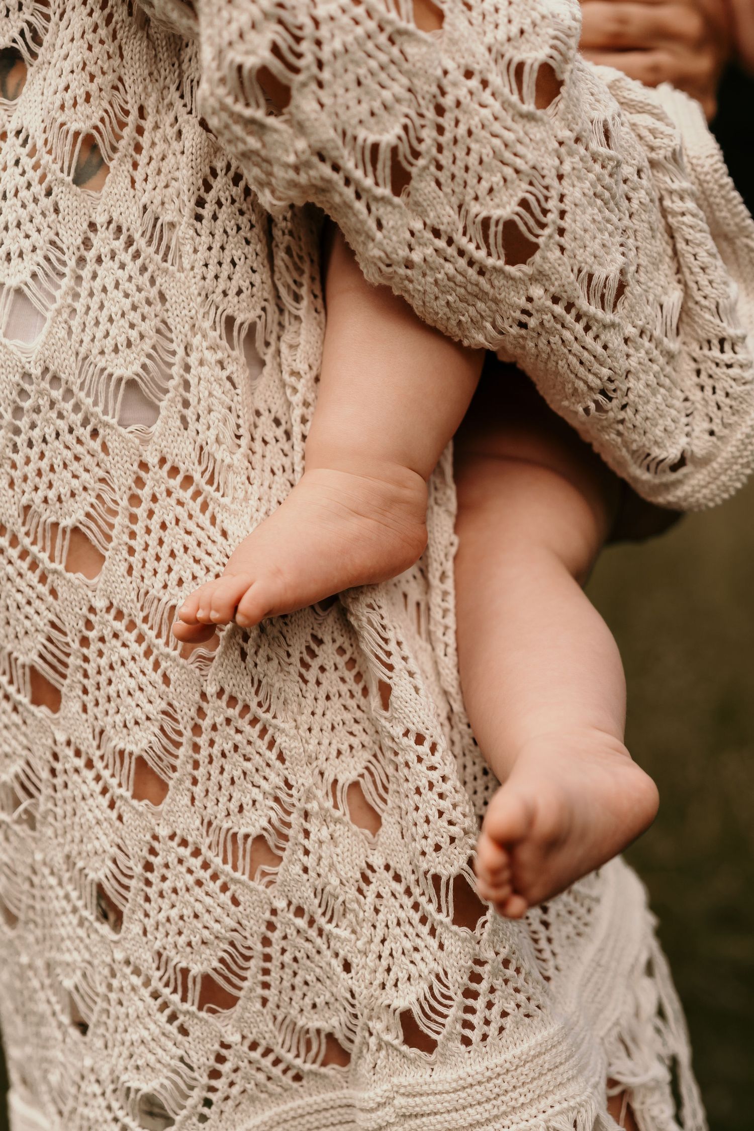 Tiny bare feet peek out from beneath cream-colored knit lace blanket with delicate openwork pattern.