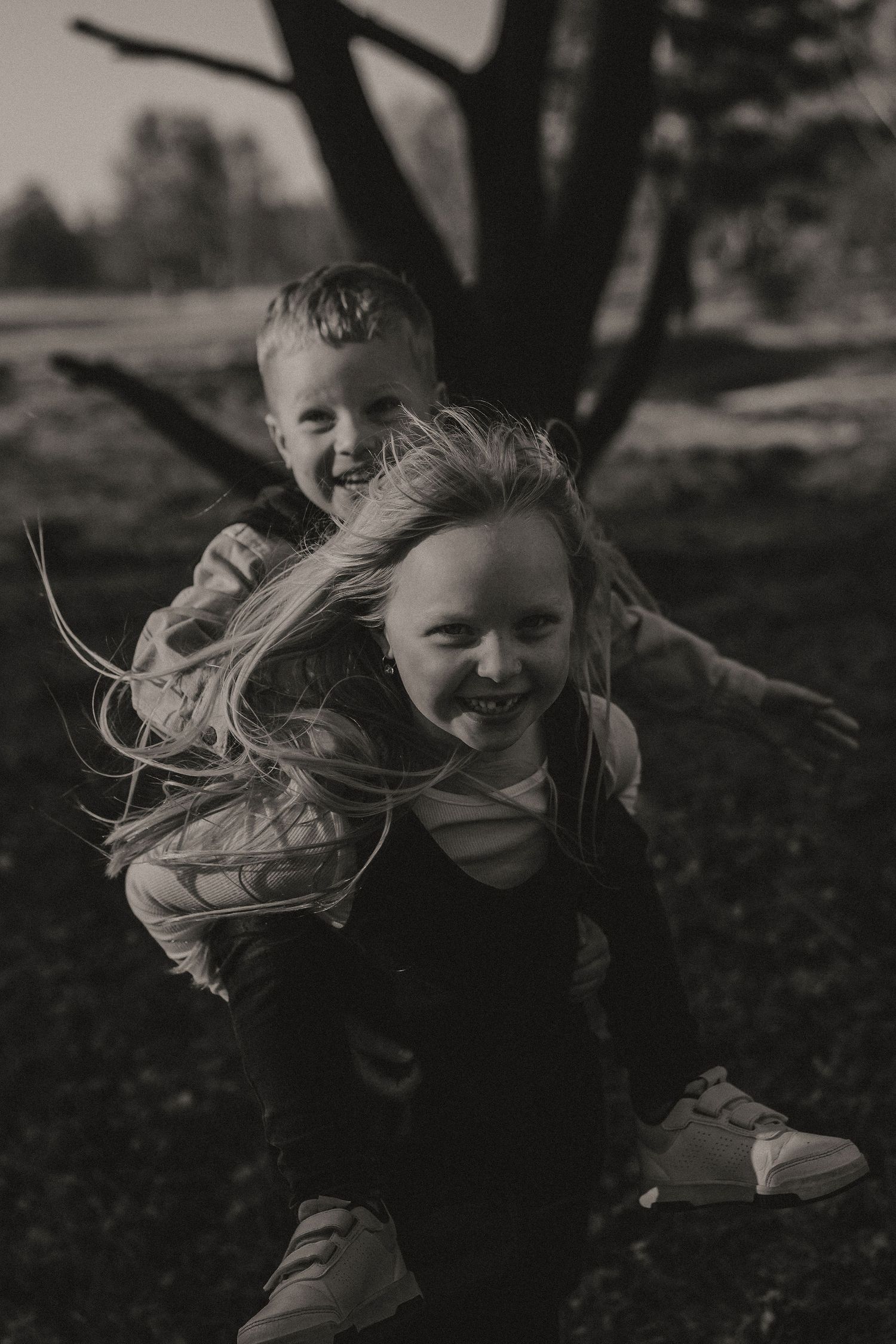Black and white photo showing a piggyback ride outdoors as hair blows in the wind on a sunny day.