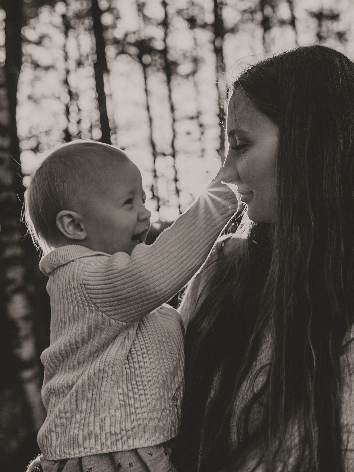 A tender black and white moment between a parent and baby in a forest setting with soft bokeh lighting.